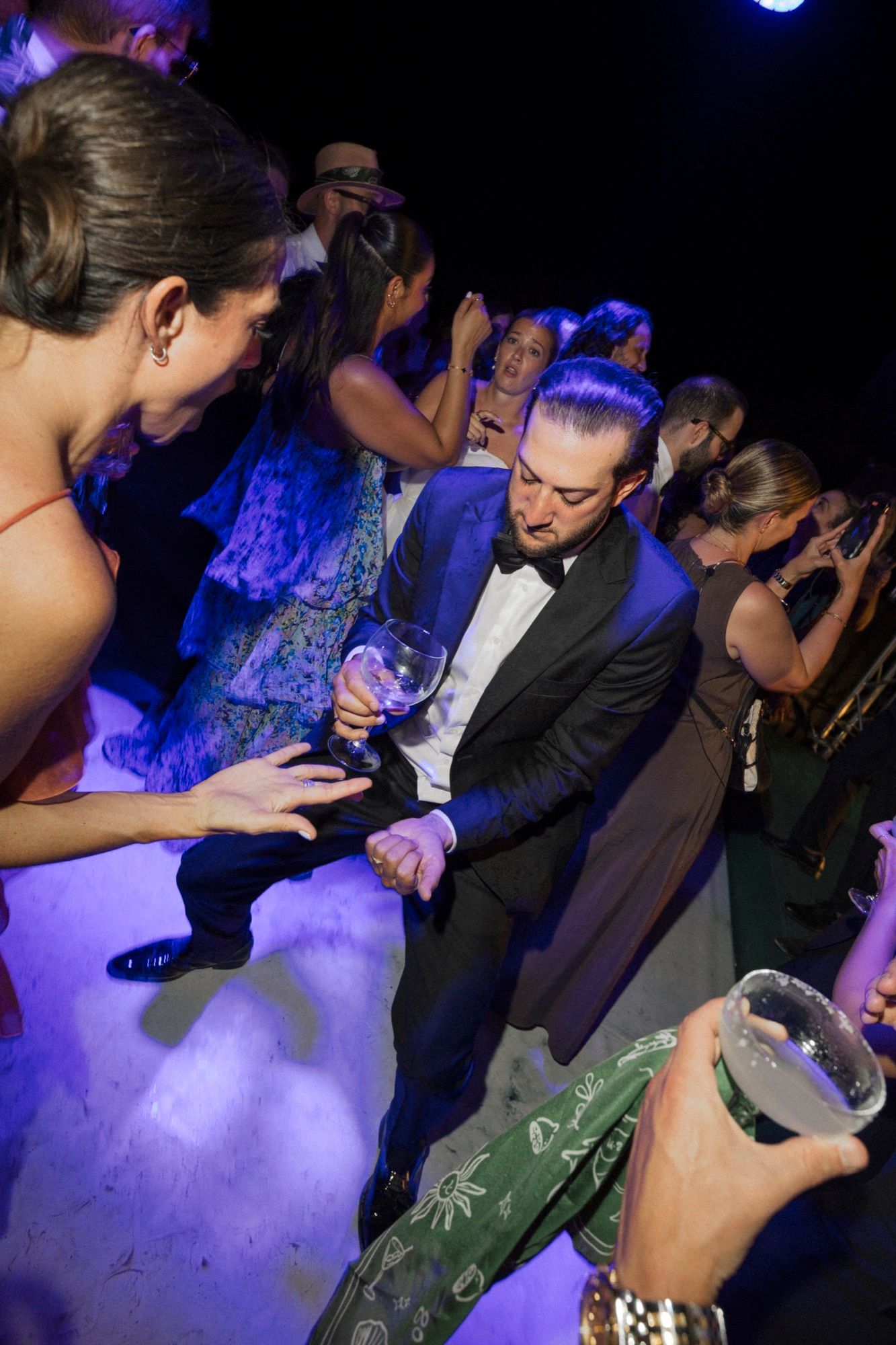Wedding party dancing under blue lighting at nighttime reception celebration.