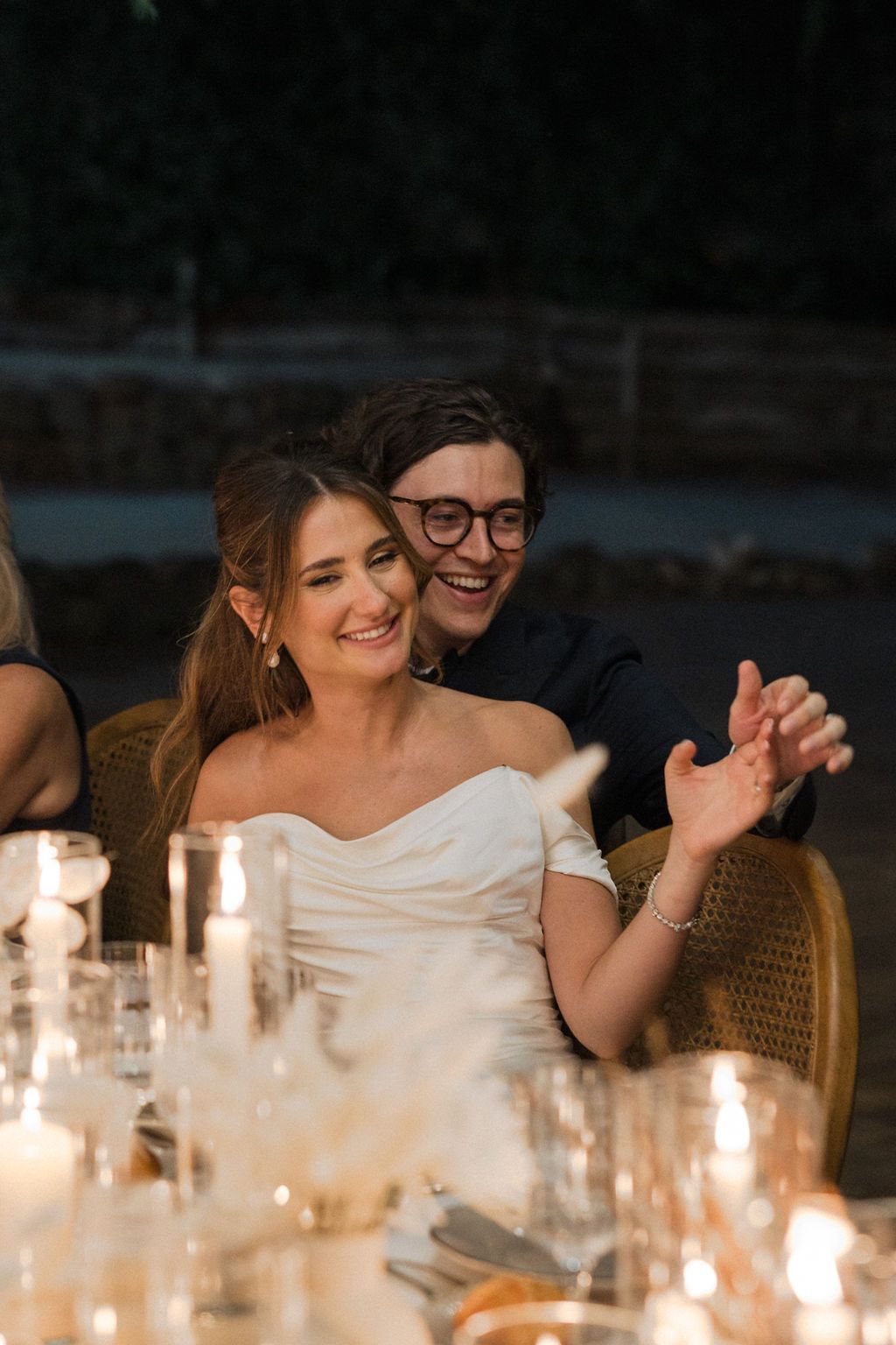 Intimate candlelit wedding reception with guests sharing laughter at dinner.