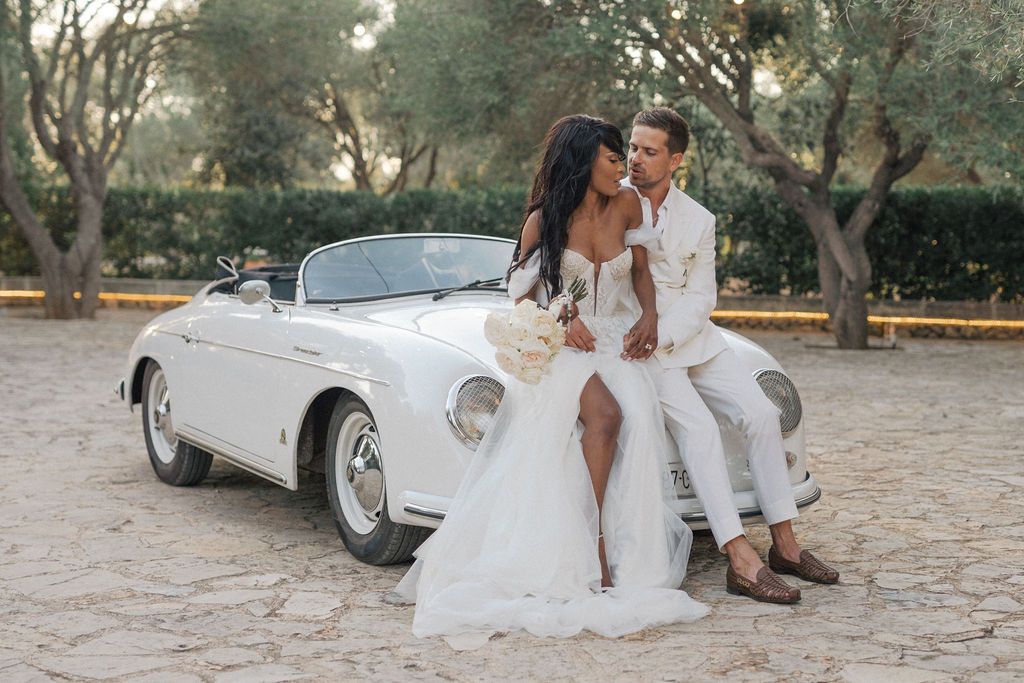Wedding couple sharing intimate moments near a classic car outdoors.