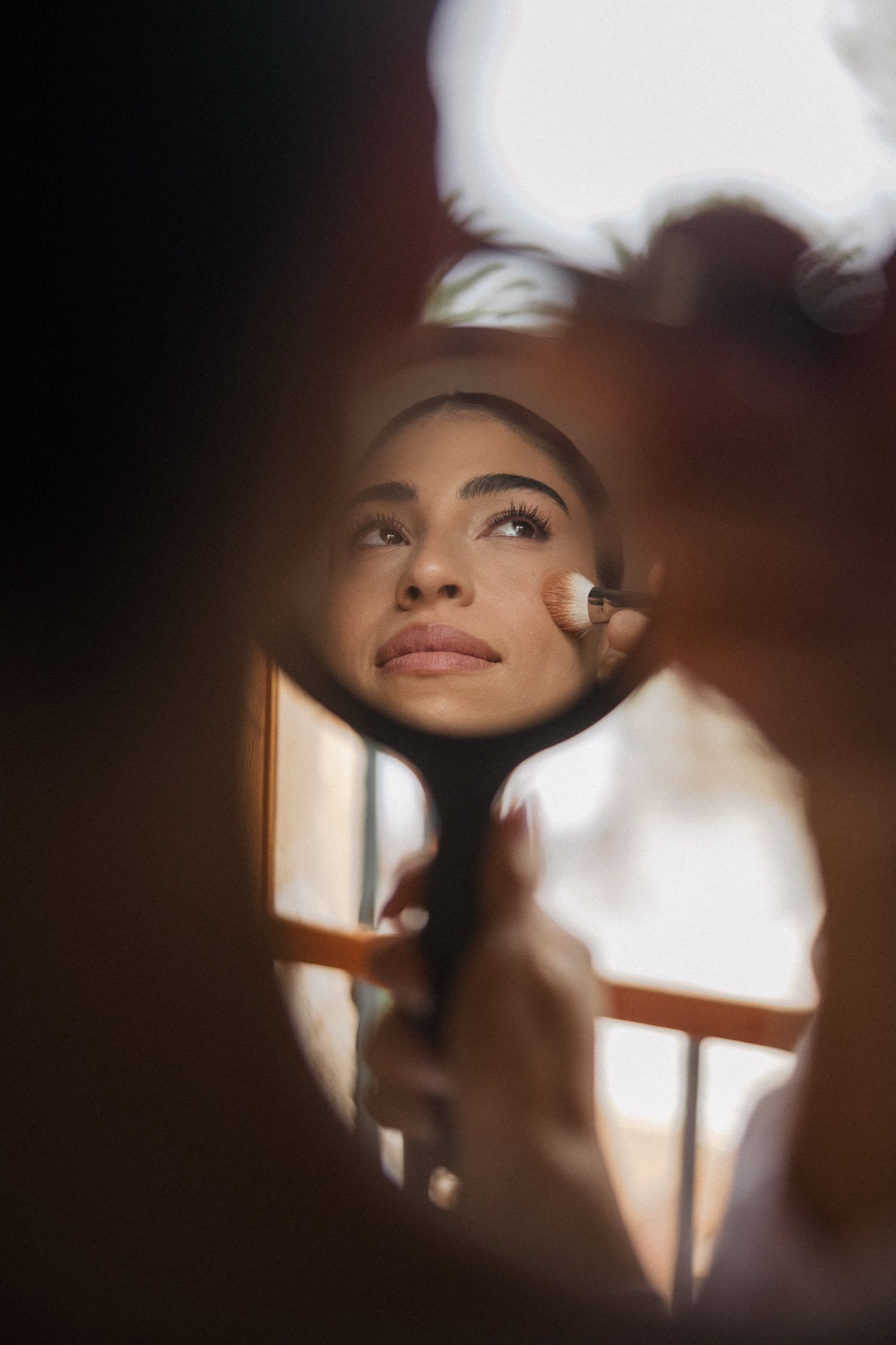 Artistic portrait shot through reflective surface with soft lighting and dreamy atmosphere.