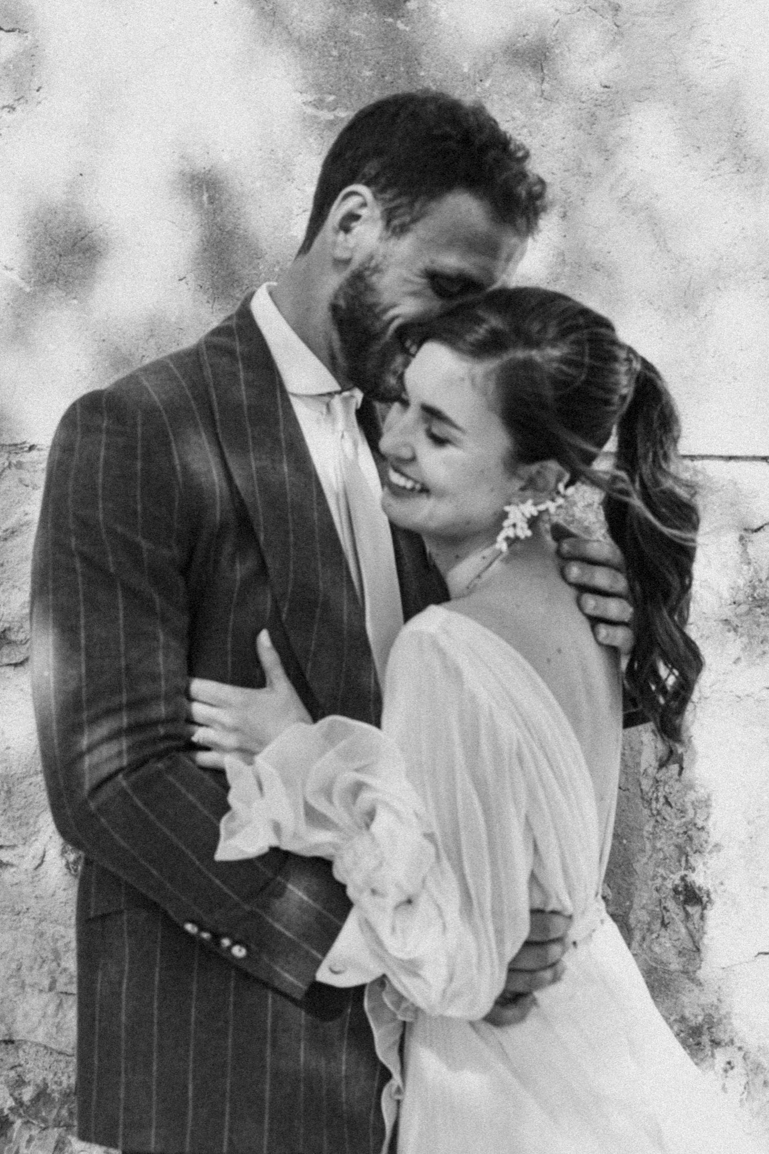 A romantic black and white photo series showing a couple in wedding attire sharing intimate kisses against a textured wall.