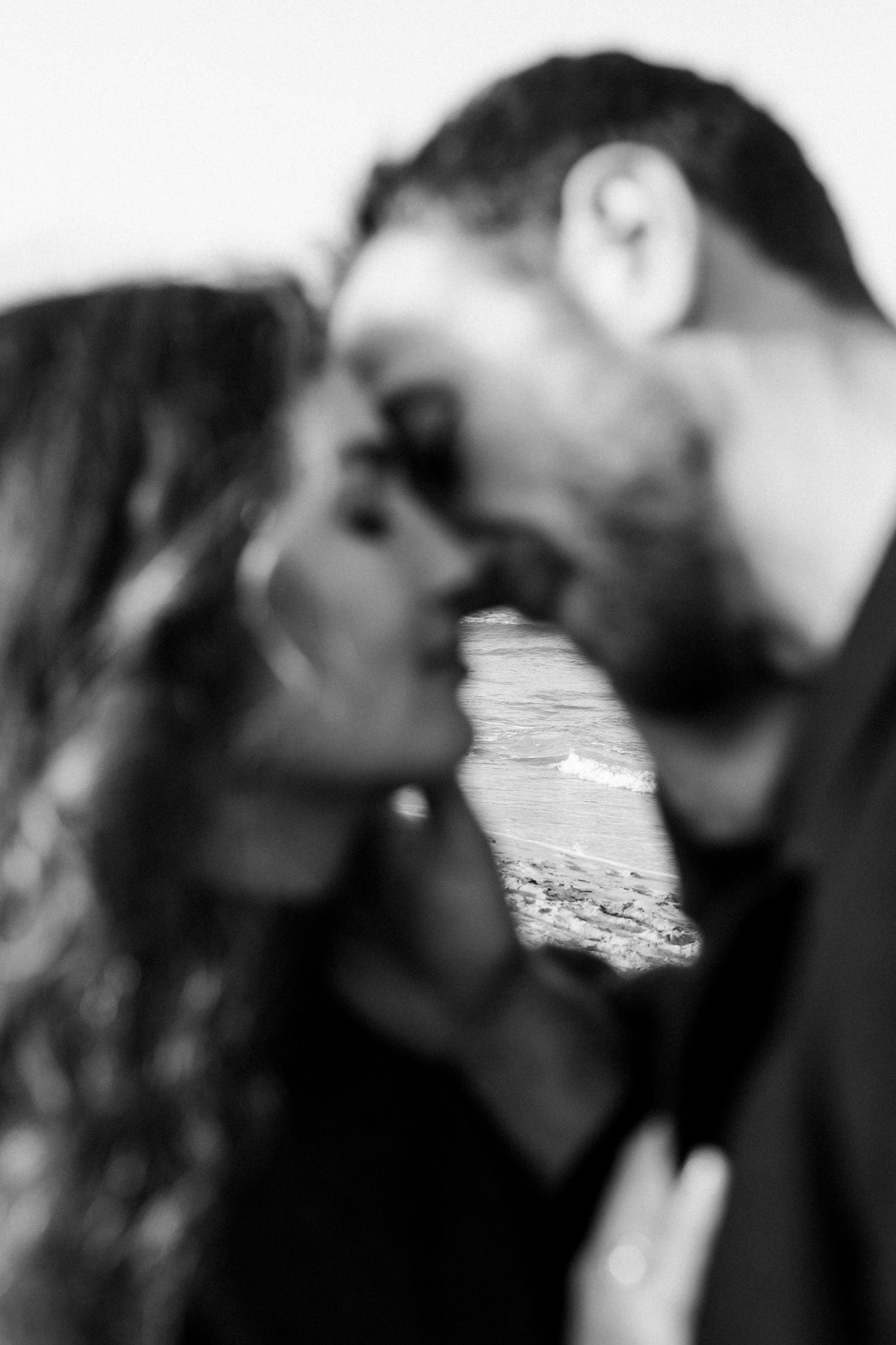 Black and white romantic portrait of a couple about to kiss with a scenic mountain landscape visible between them.