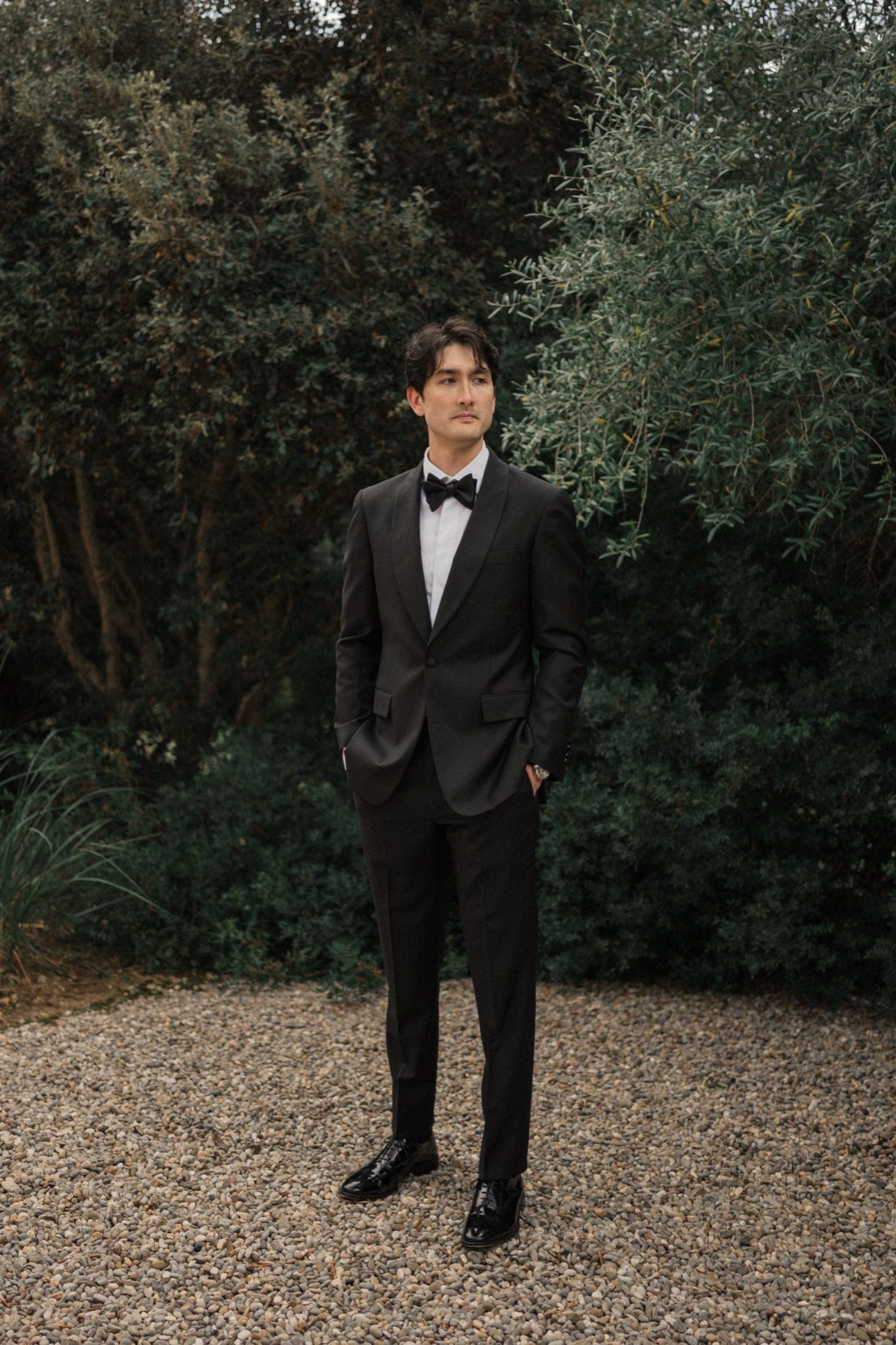 A formal portrait session outdoors showing a black tuxedo against a natural wooded background.