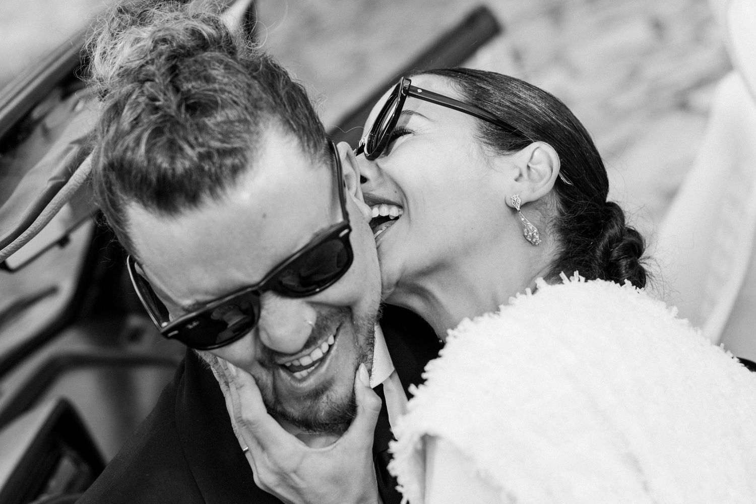 A couple wearing sunglasses shares a joyful moment during their wedding celebration.
