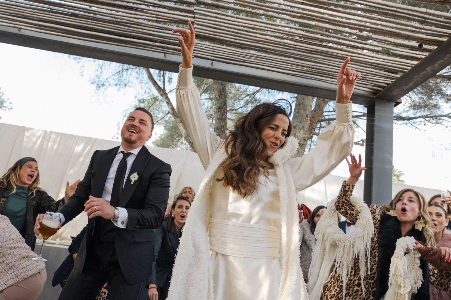 Joyful wedding celebration with guests and couple raising hands in outdoor setting.