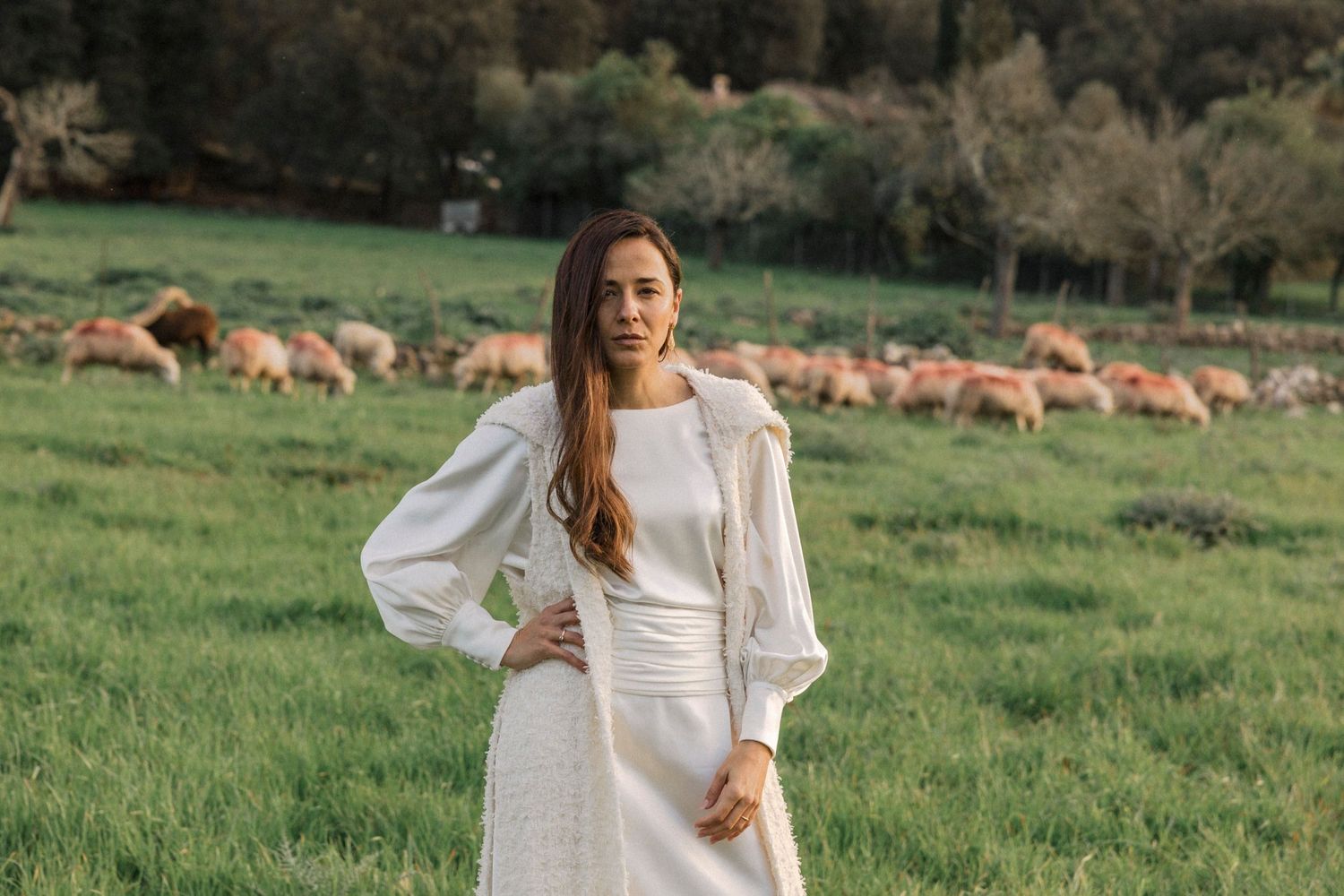 A white wedding dress with billowing sleeves stands out against a pastoral landscape with grazing sheep.