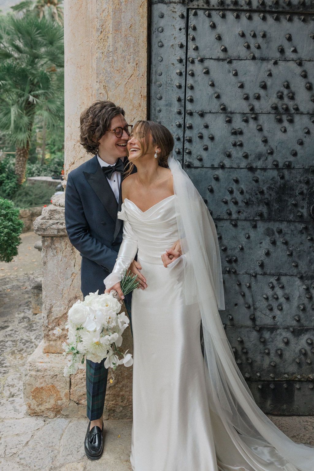 Romantic wedding moment captured against rustic stone wall and ornate metal door.