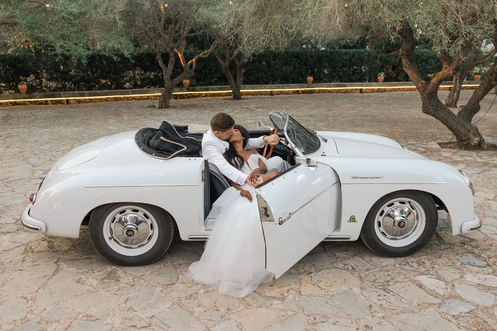 Classic white vintage convertible car parked in Mediterranean garden setting.