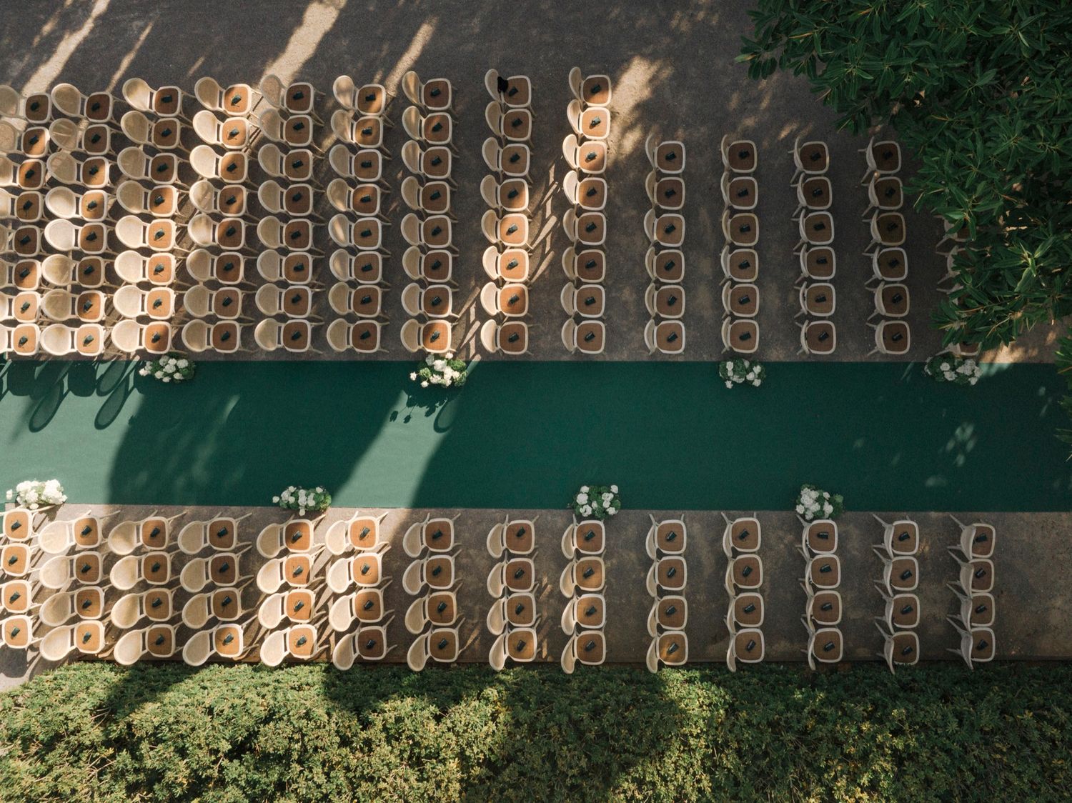 Aerial view of wedding ceremony seating arrangement with rows of chairs along a green carpet aisle.