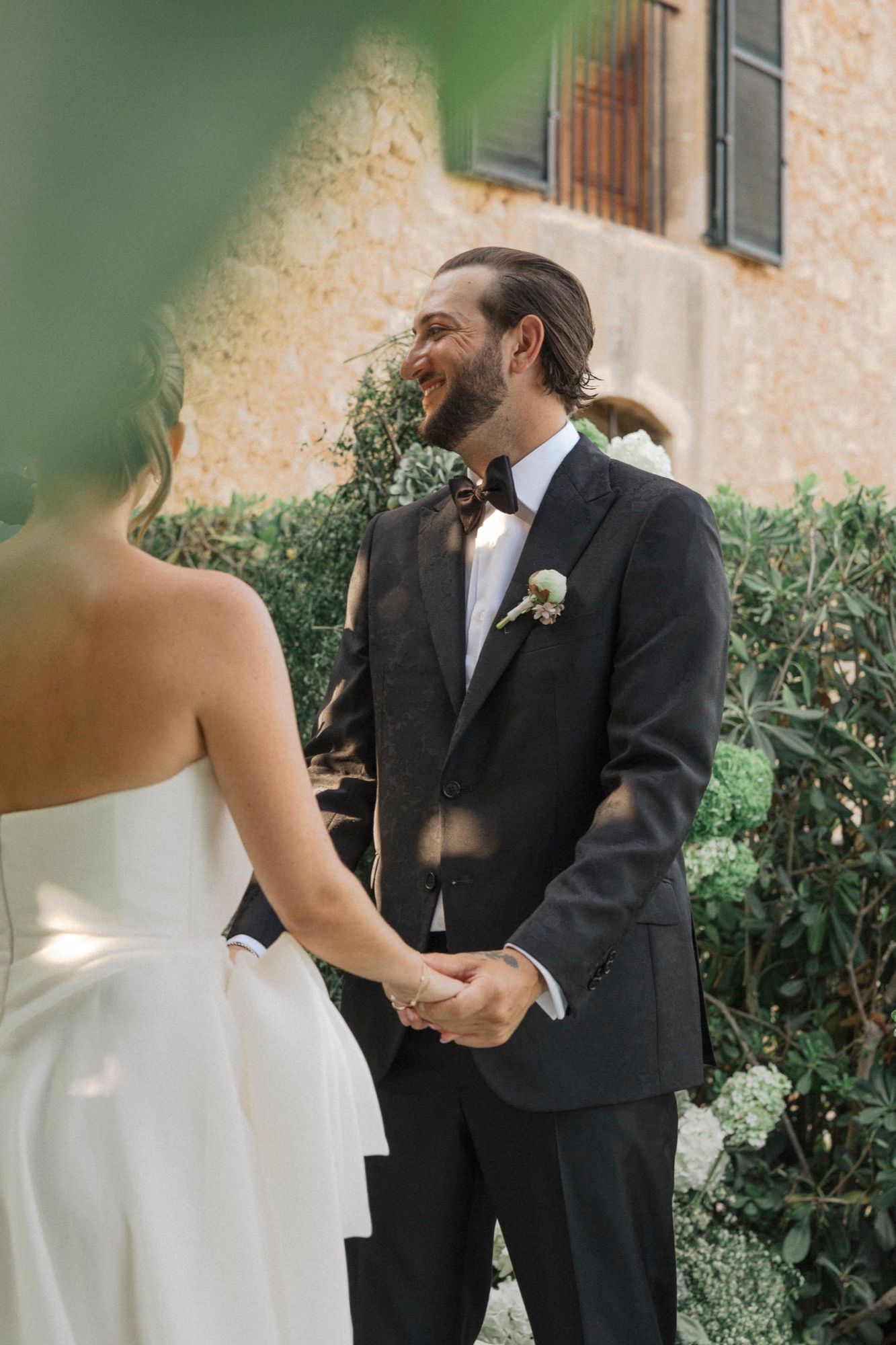 Intimate wedding moment captured against a rustic stone wall with greenery in the background.