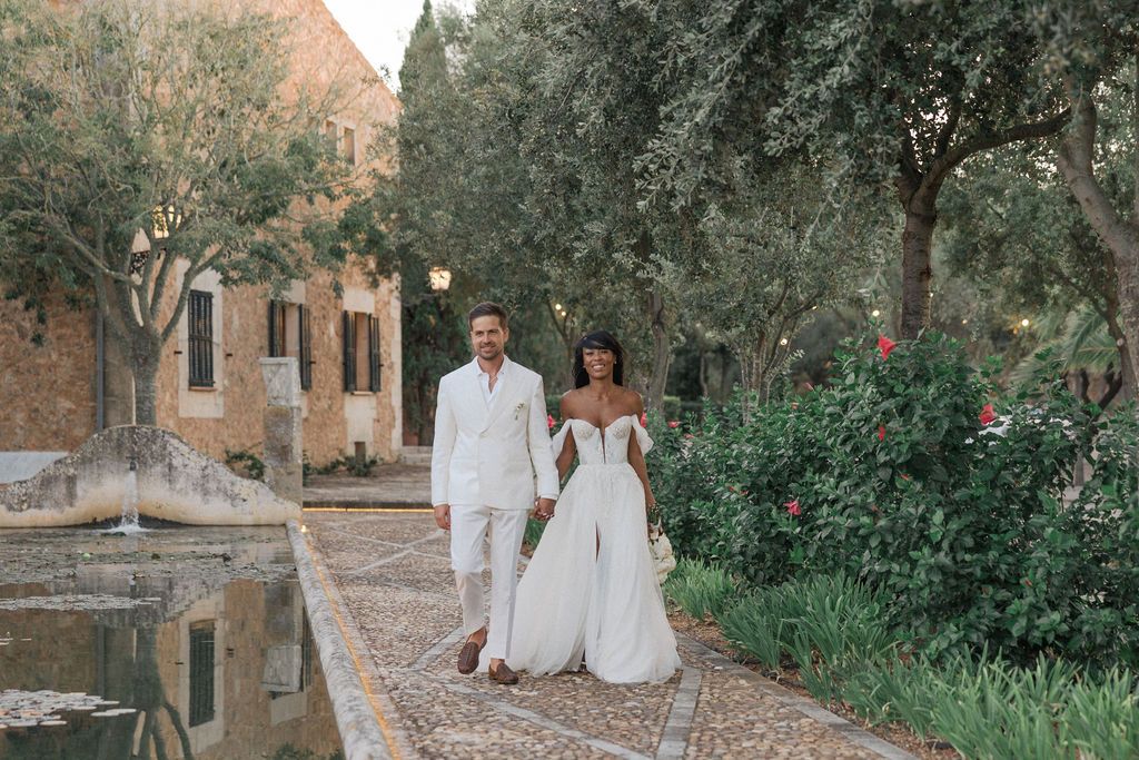 Wedding couple walking along stone path surrounded by olive trees and cypress.