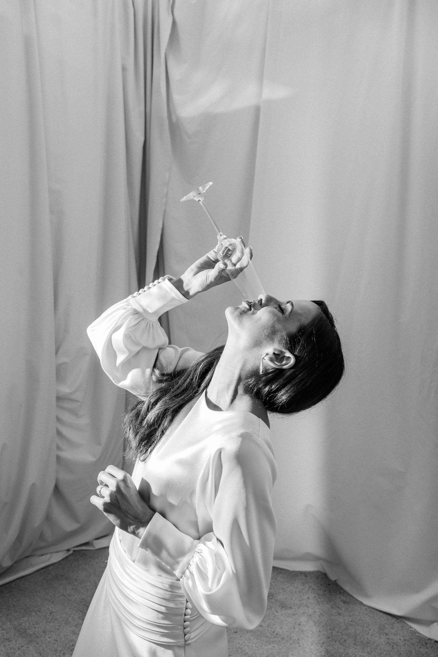 A person in white dramatically tilts back while drinking from a champagne glass.
