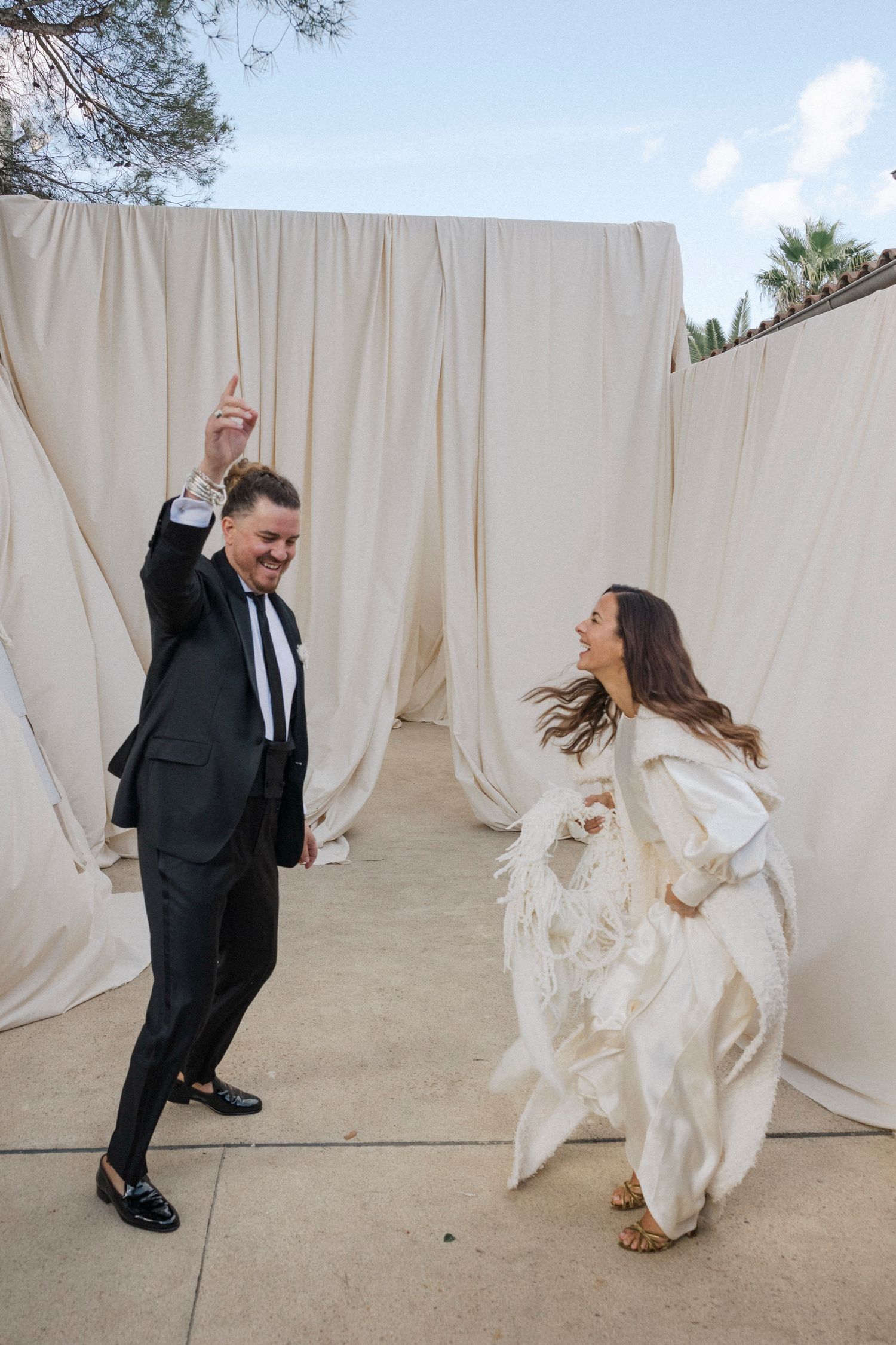 A couple dances playfully between white curtains at an outdoor wedding venue.