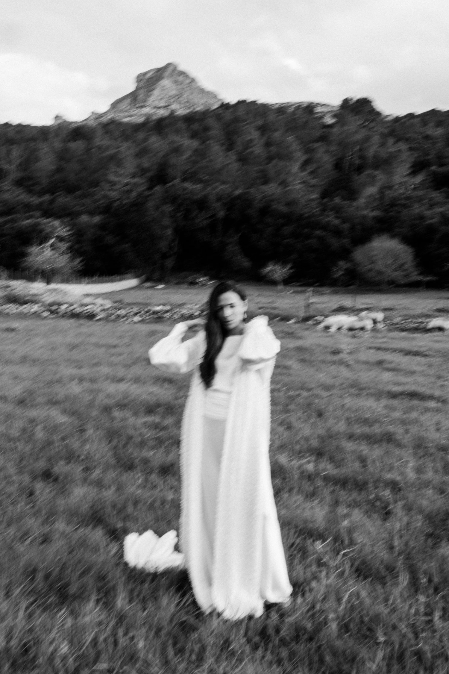 Person in flowing white dress twirls dramatically in a mountain meadow.