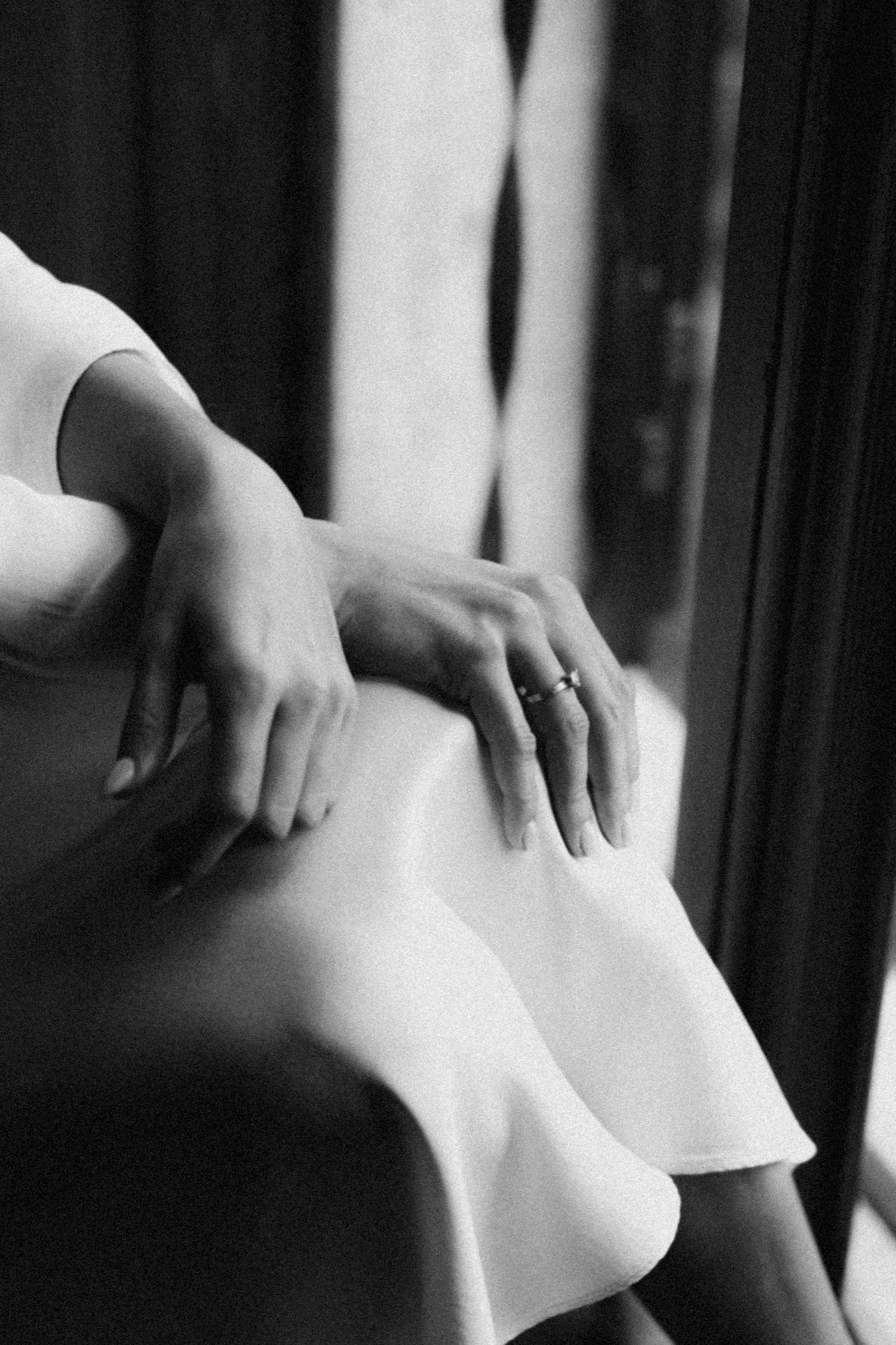 Elegant hands delicately grasp white fabric in an artistic black and white composition.
