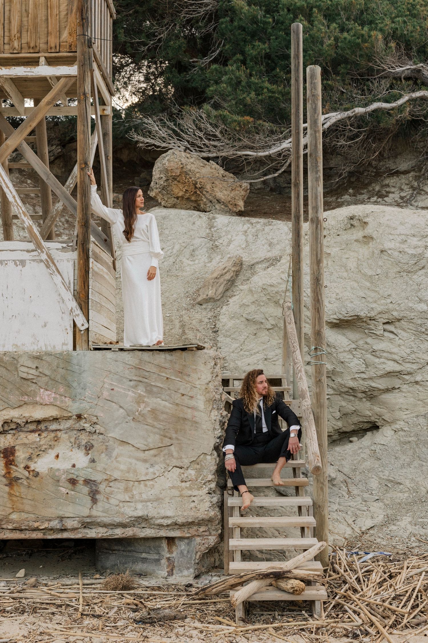 Two people pose on rustic wooden stairs against rocky cliff backdrop.