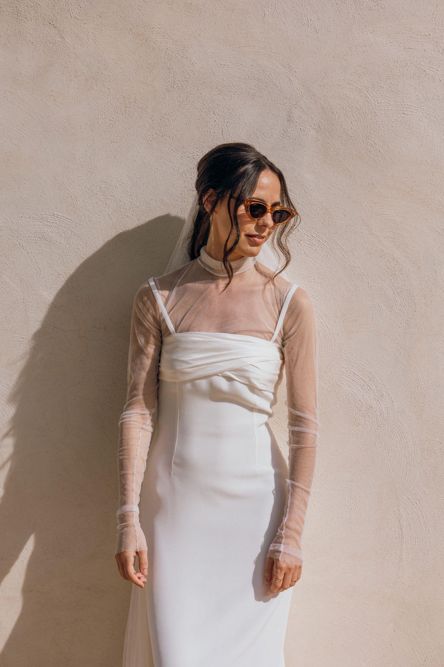 Four fashion photos showing a white dress with sheer mesh long sleeves against a neutral wall in different poses.