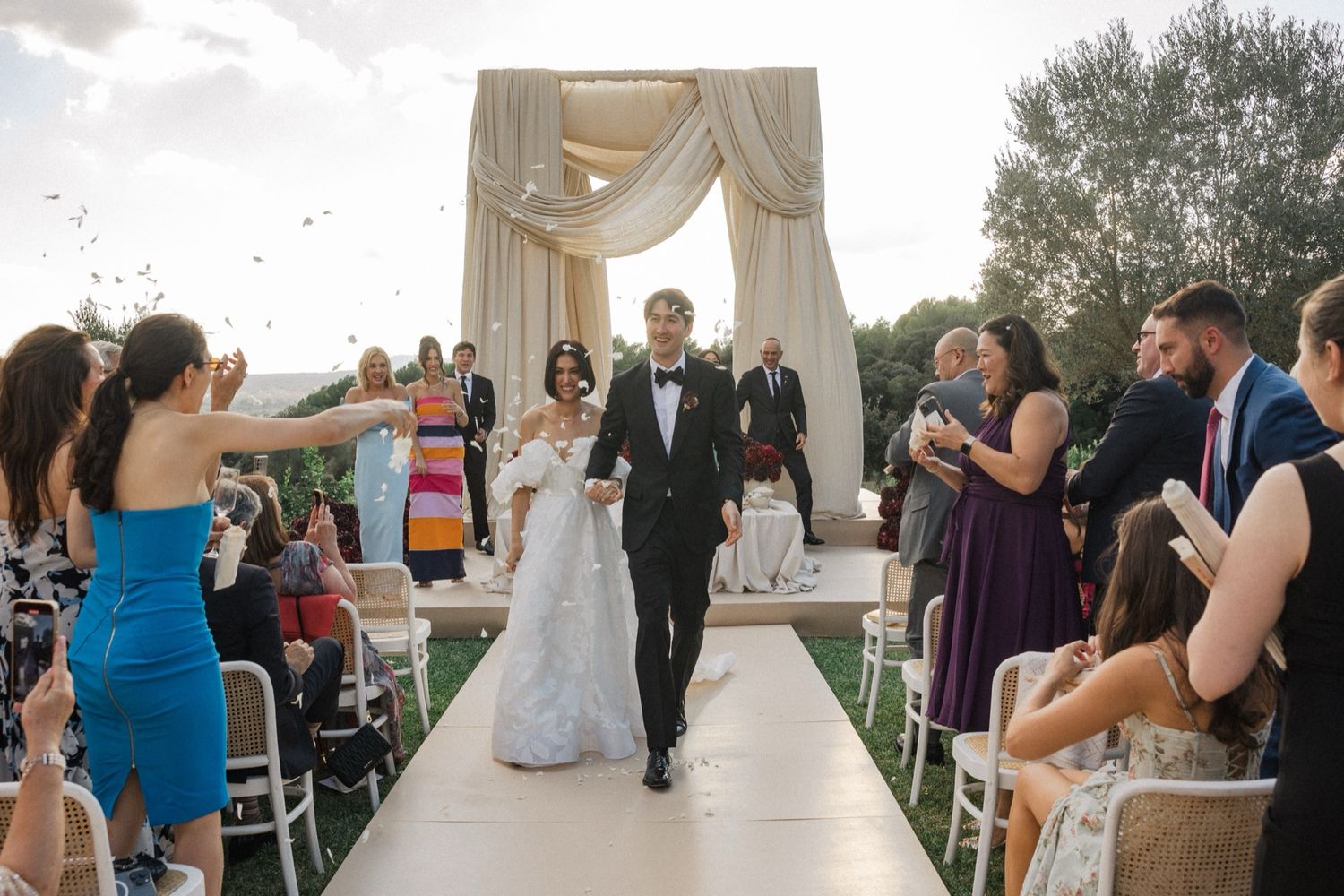 Wedding ceremony setup with elegant draping and guests seated outdoors.