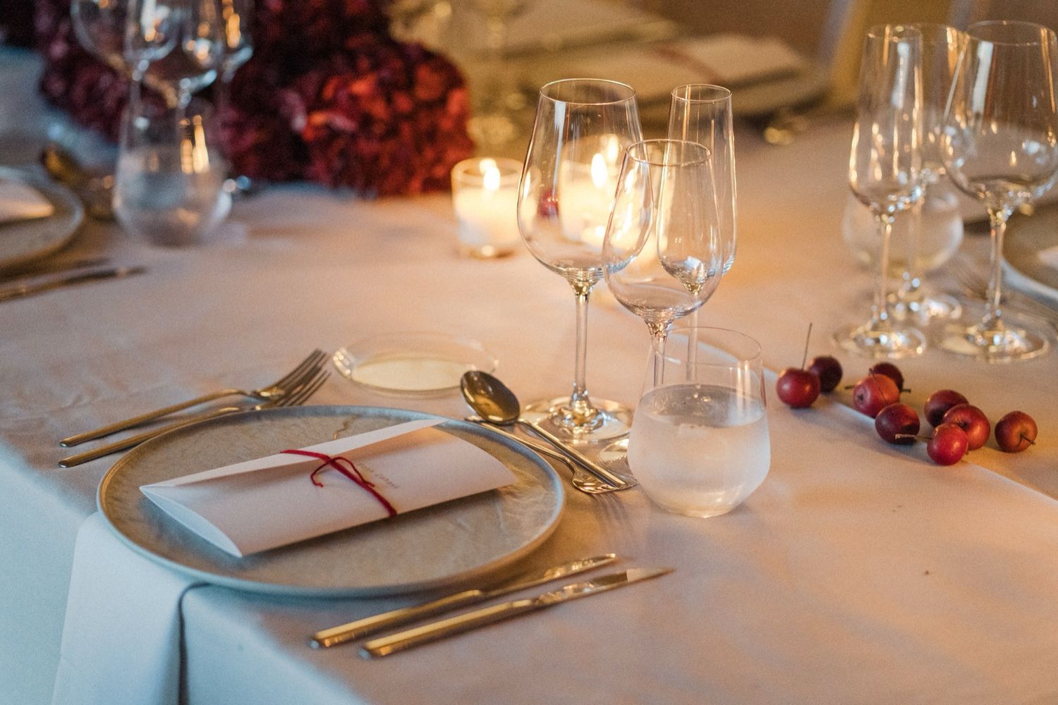 An elegant table setting with white linens, wine glasses, and gold utensils in warm candlelight.