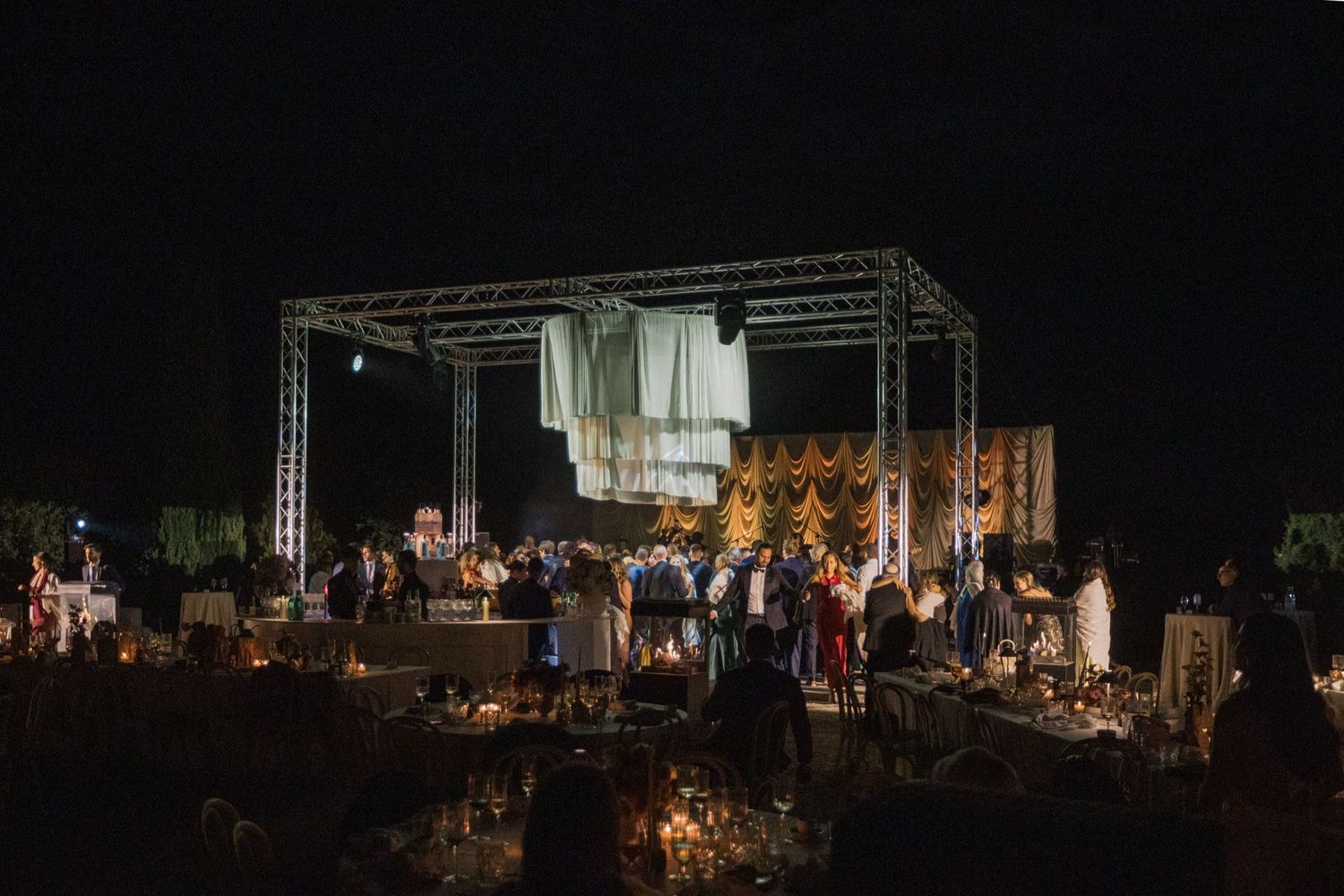 A nighttime outdoor concert setup with stage lighting and equipment on a dark background.