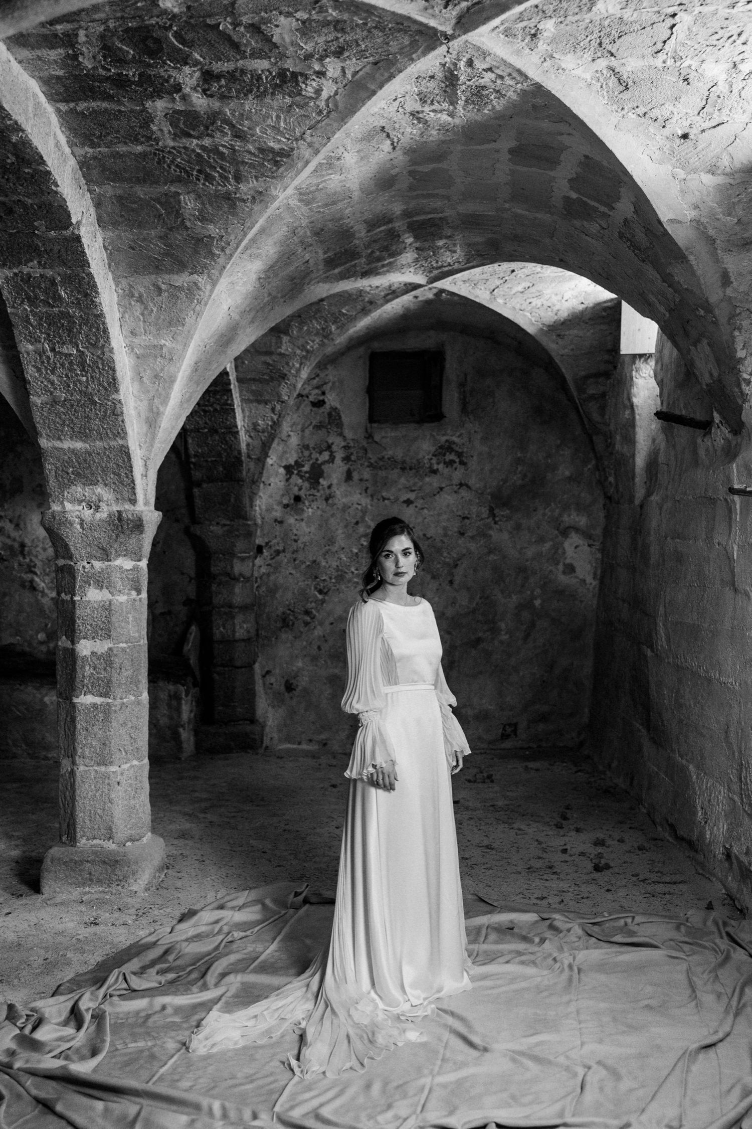 Five haunting black and white photographs show figures in white dresses standing in ancient stone catacombs.