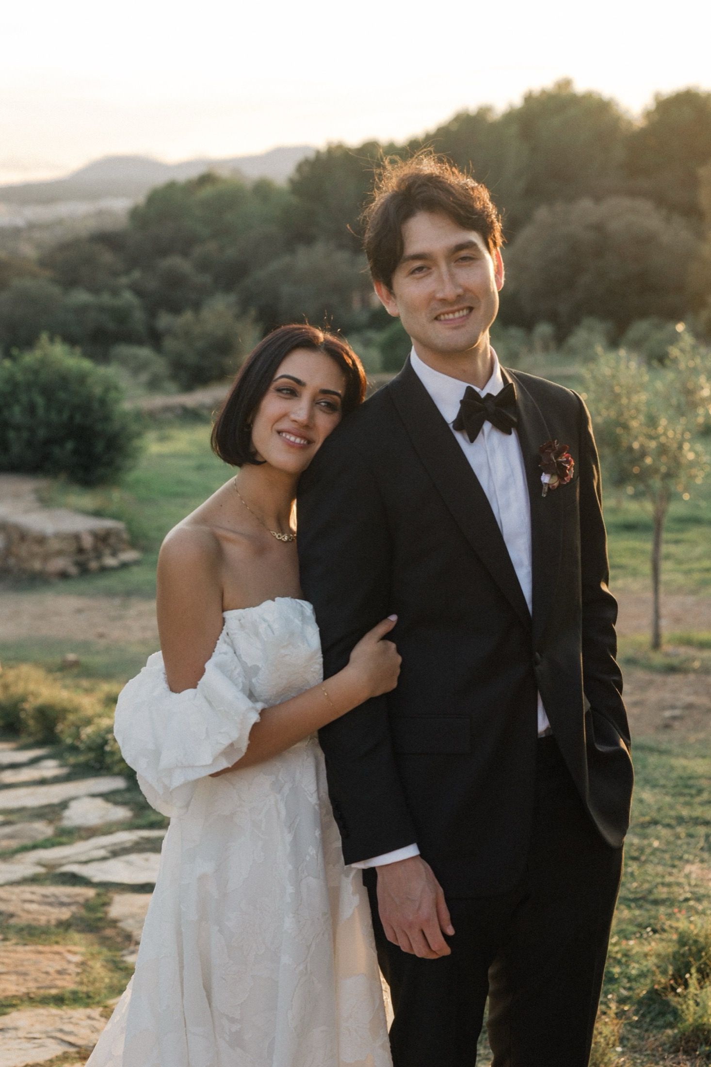 A romantic wedding photoshoot at sunset in a rustic outdoor setting with rolling hills in the background.