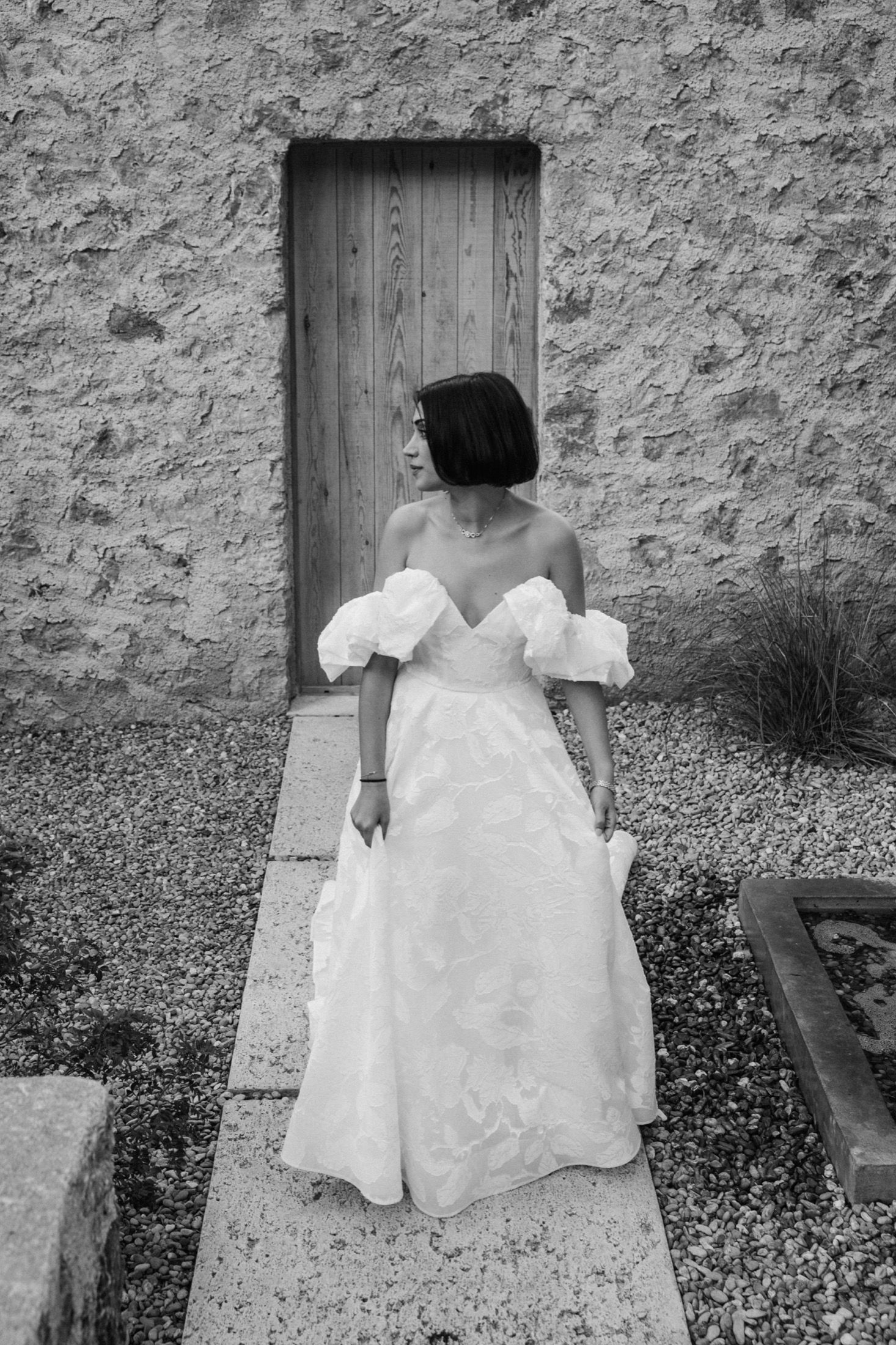 A series of black and white photographs showing someone in a white dress sitting on a stone bench against a textured wall.