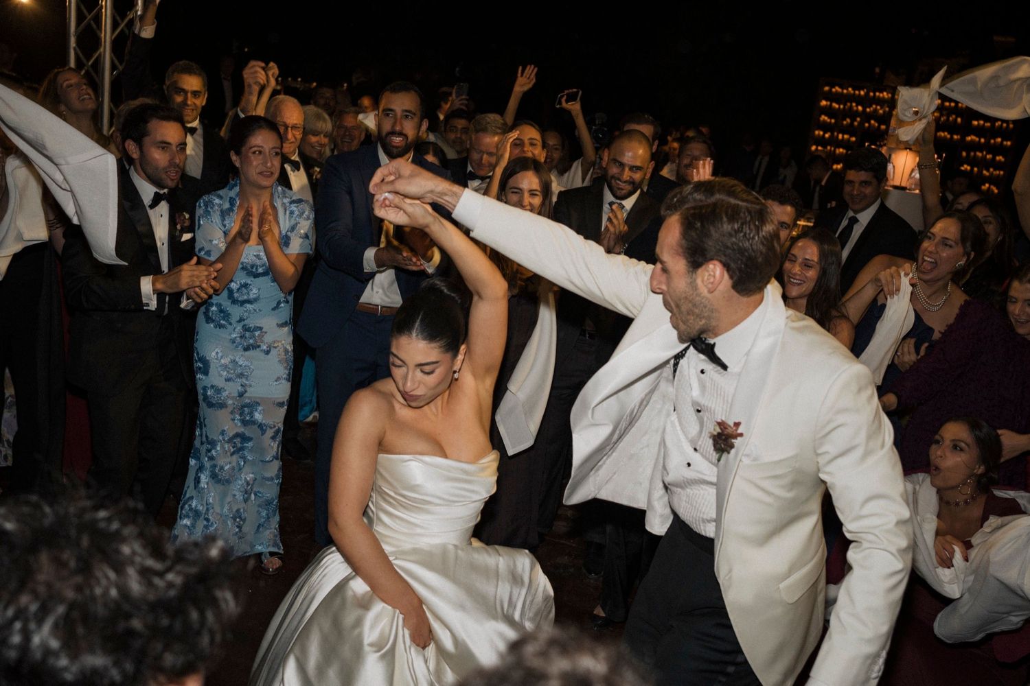 Wedding guests dance and celebrate together on a crowded dance floor at an evening reception.