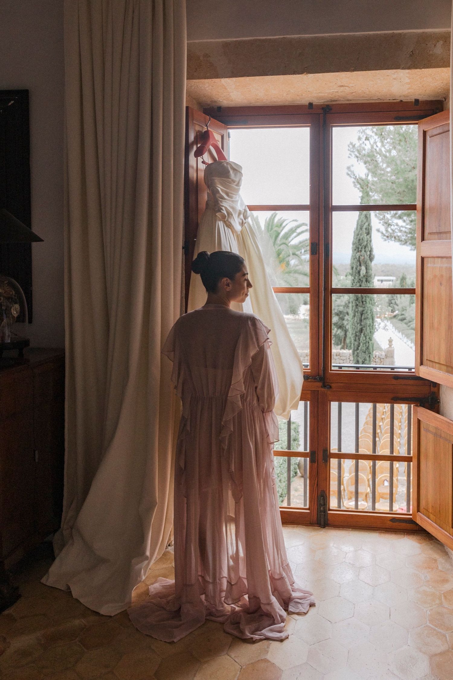 Ethereal silhouettes of flowing dresses stand against sunlit windows in a bright interior space.