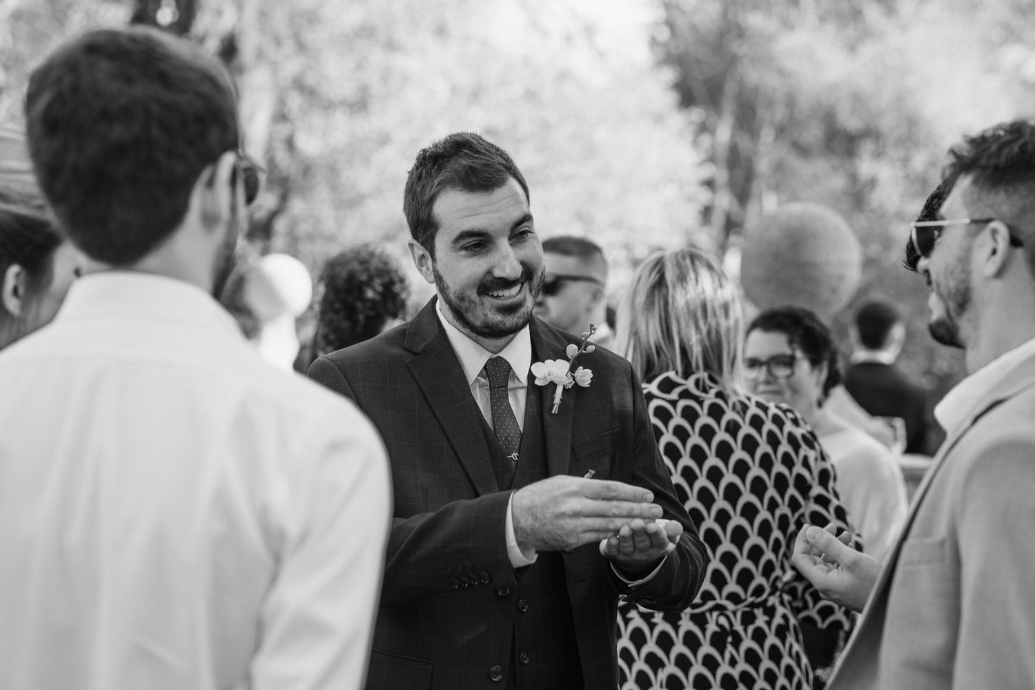 A candid black and white photo of guests mingling at an outdoor social gathering.
