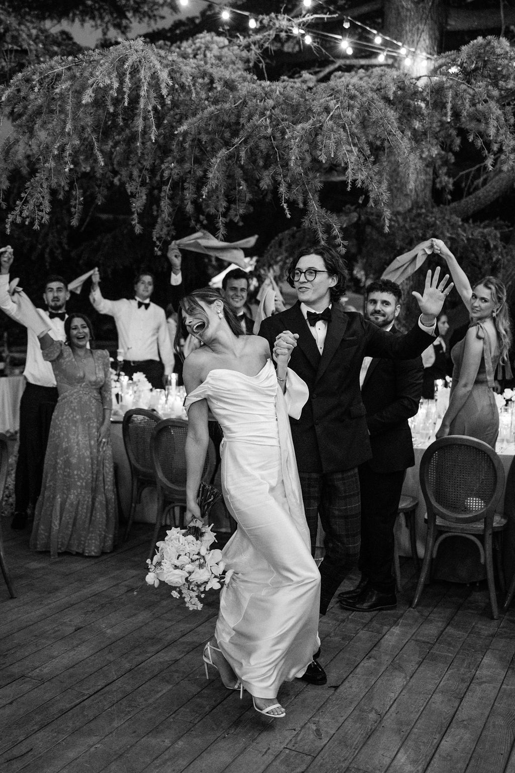 Wedding celebration on outdoor dance floor with guests dancing under trees.