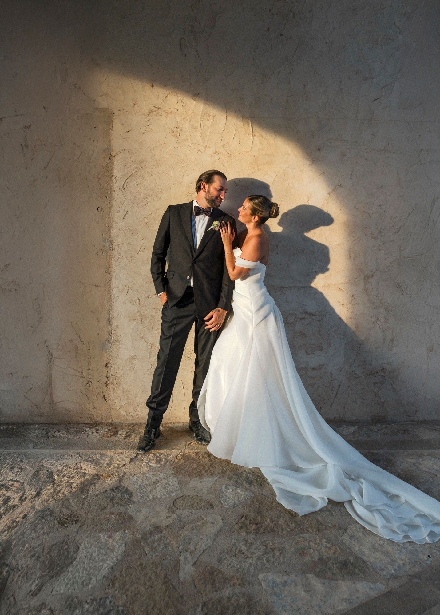 A stylish wedding portrait with dramatic lighting as couple poses against a stone wall.