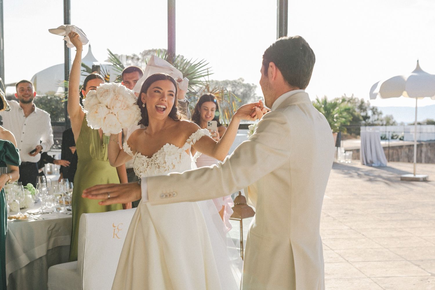 Bride and groom share a joyful first dance at an elegant outdoor wedding reception with guests celebrating.