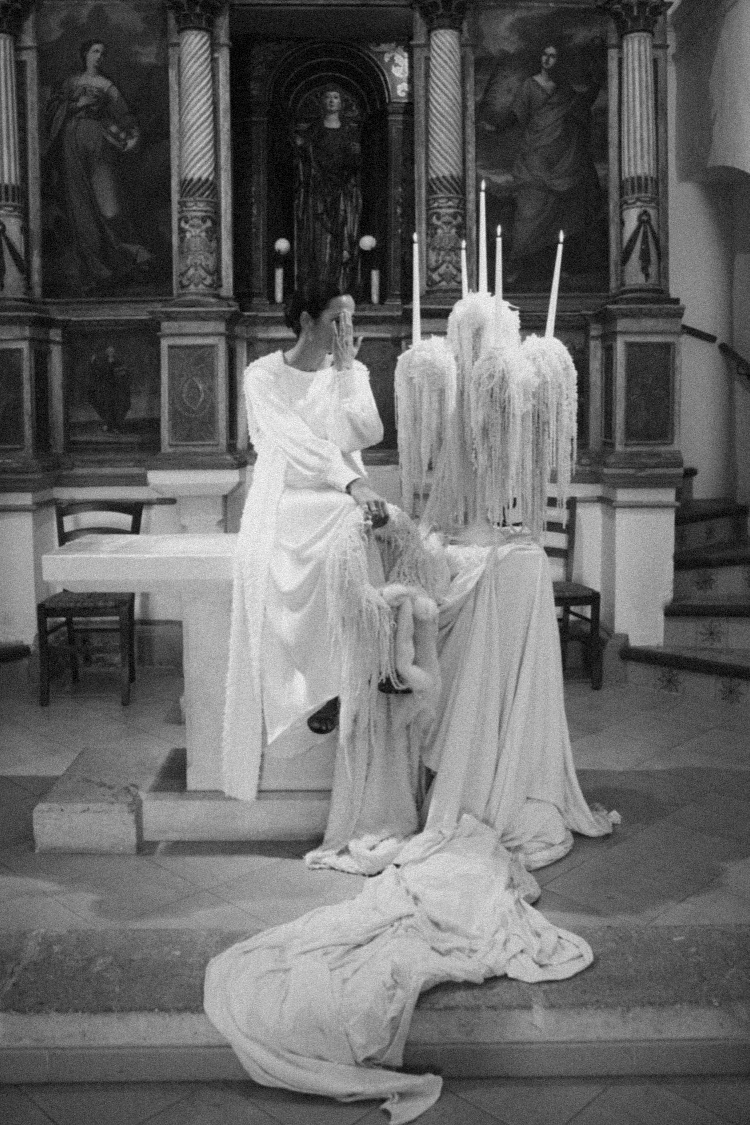 Black and white photo of elegant white draped fabric and candles in an ornate church setting.