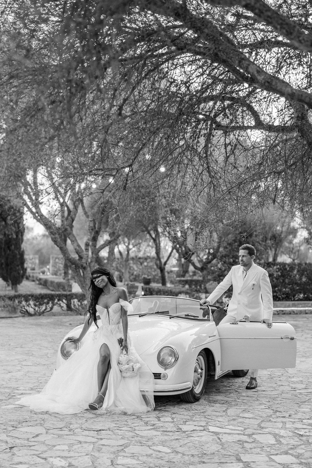 Black and white photo series of a couple in wedding attire posing near a vintage car under trees.