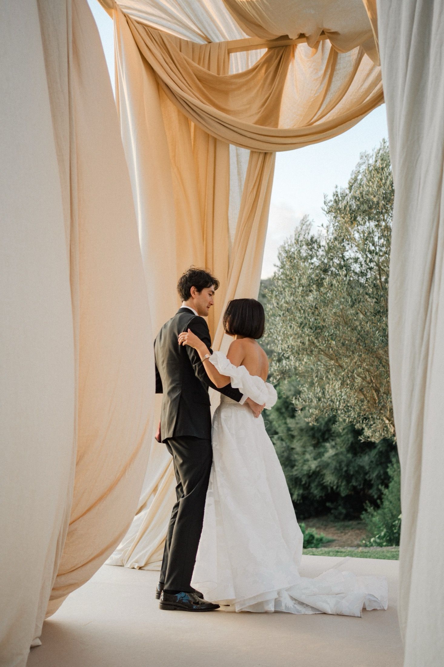 Elegant wedding scene with flowing champagne-colored drapes and a couple dancing in a light-filled space.