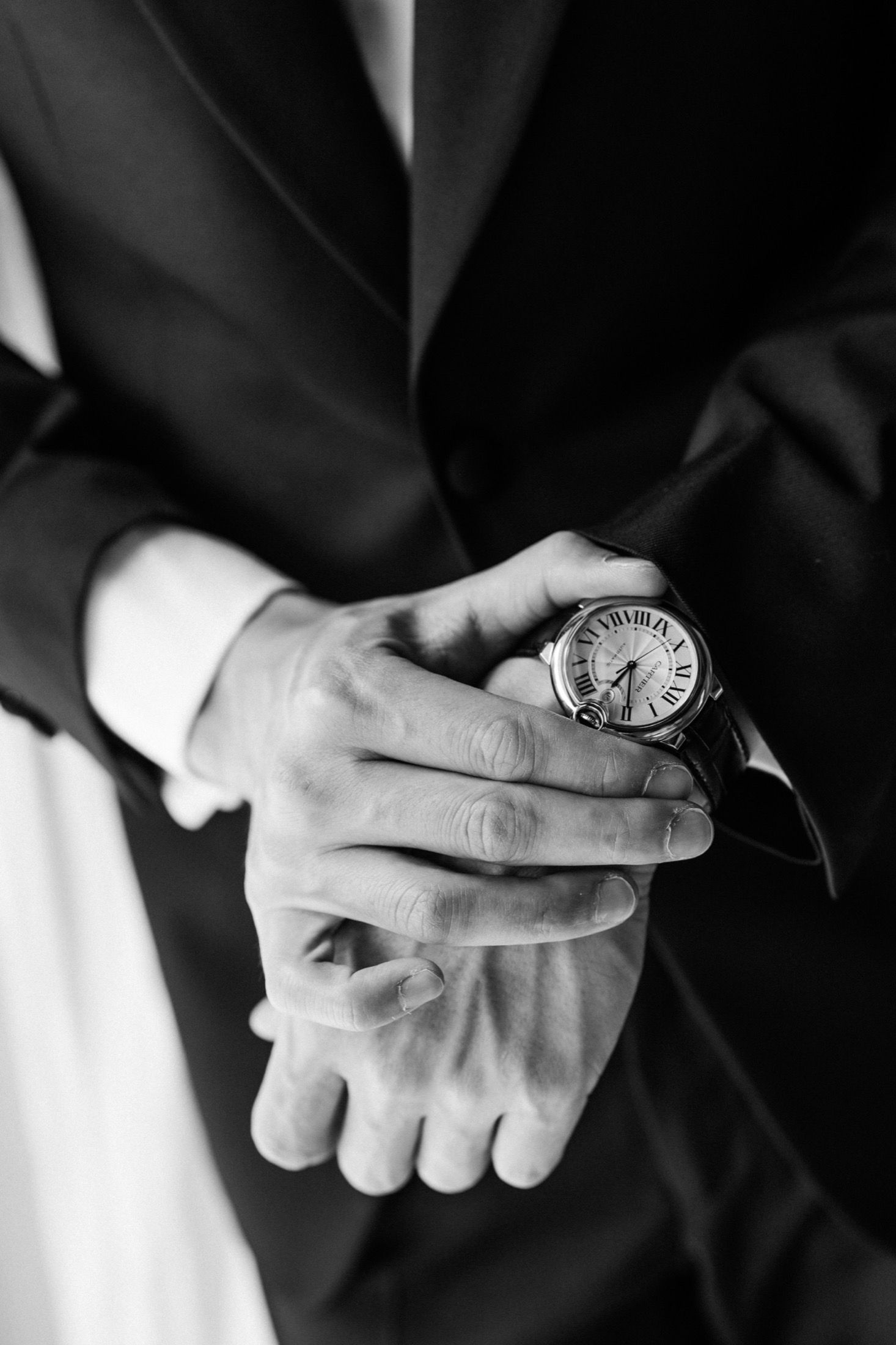 Black and white close-up of hands holding a vintage pocket watch against formal attire.