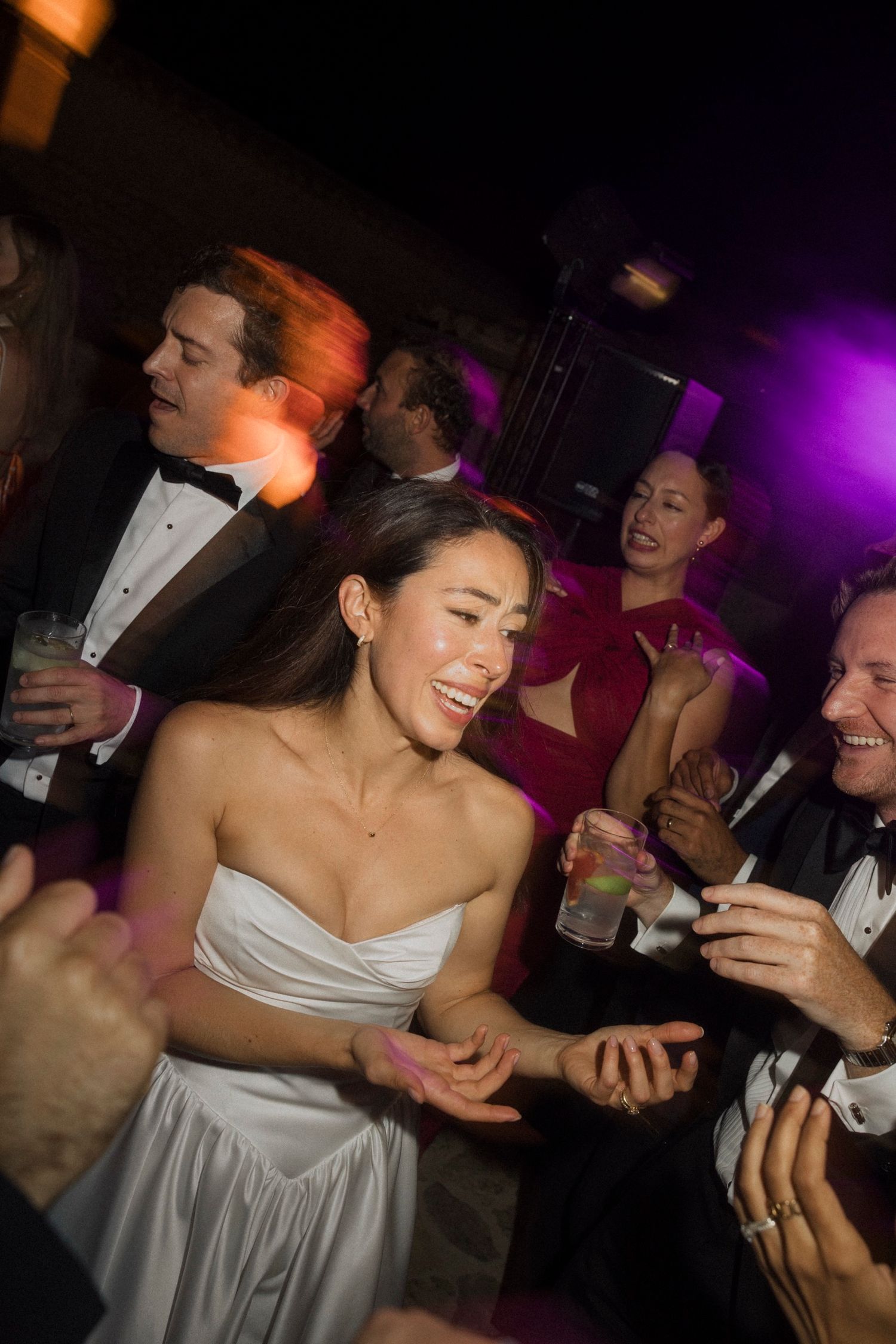 A bride in a white strapless dress dances and celebrates with guests at a wedding reception.