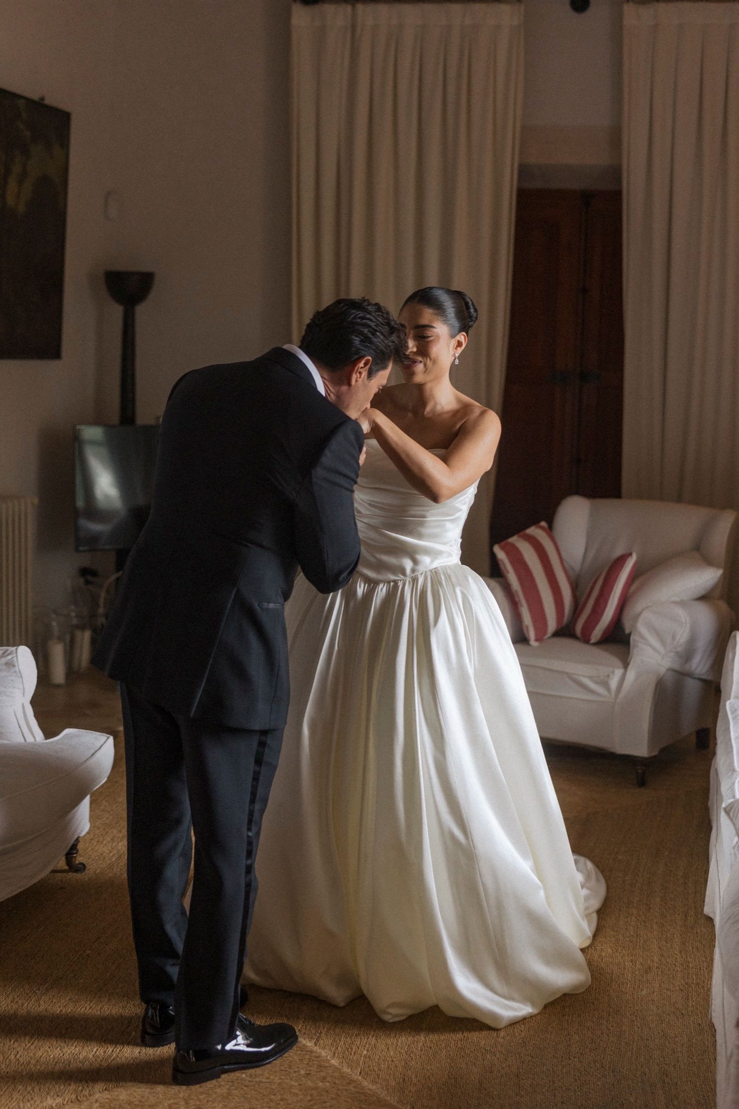 A couple shares an intimate moment in a living room, with the bride wearing a stunning white ballgown wedding dress.