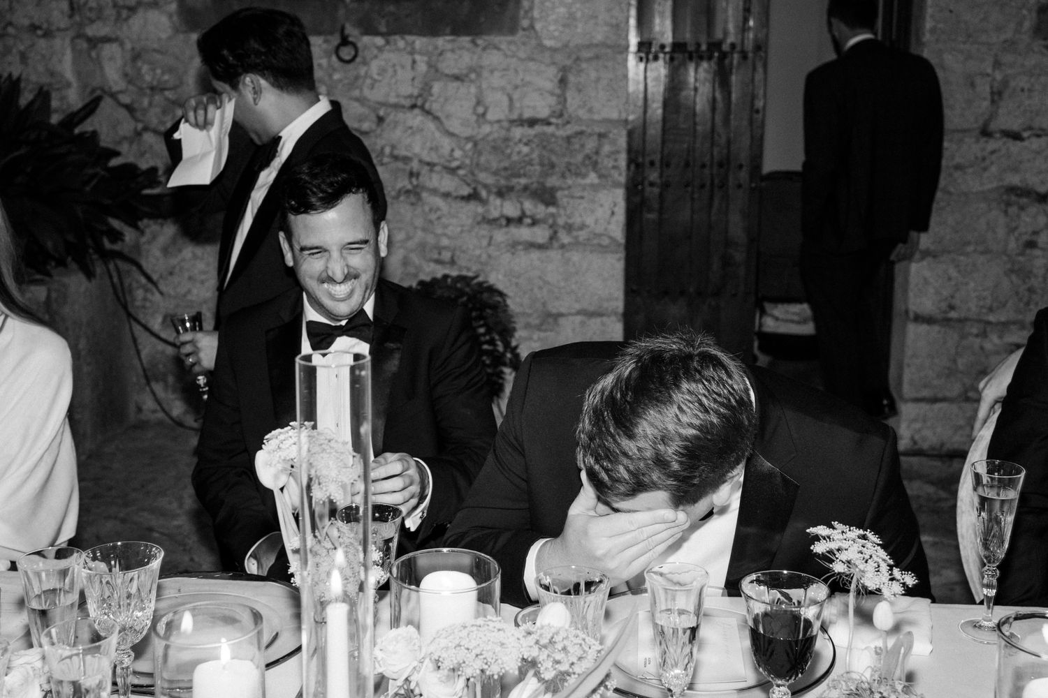 Black and white photograph of a formal dinner party with guests seated at long tables in an elegant stone interior.