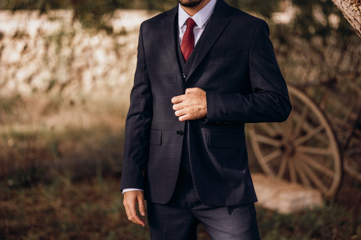 Close-up view of a formal black suit with red tie against a blurred outdoor background.