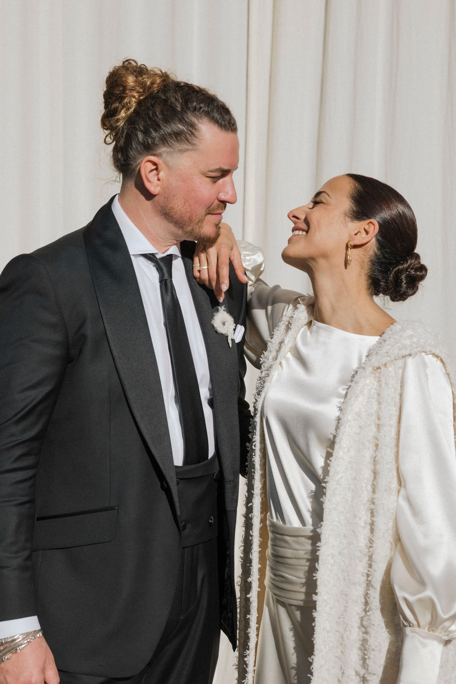 Candid wedding moment showing joyful laughter in formal attire against white backdrop.