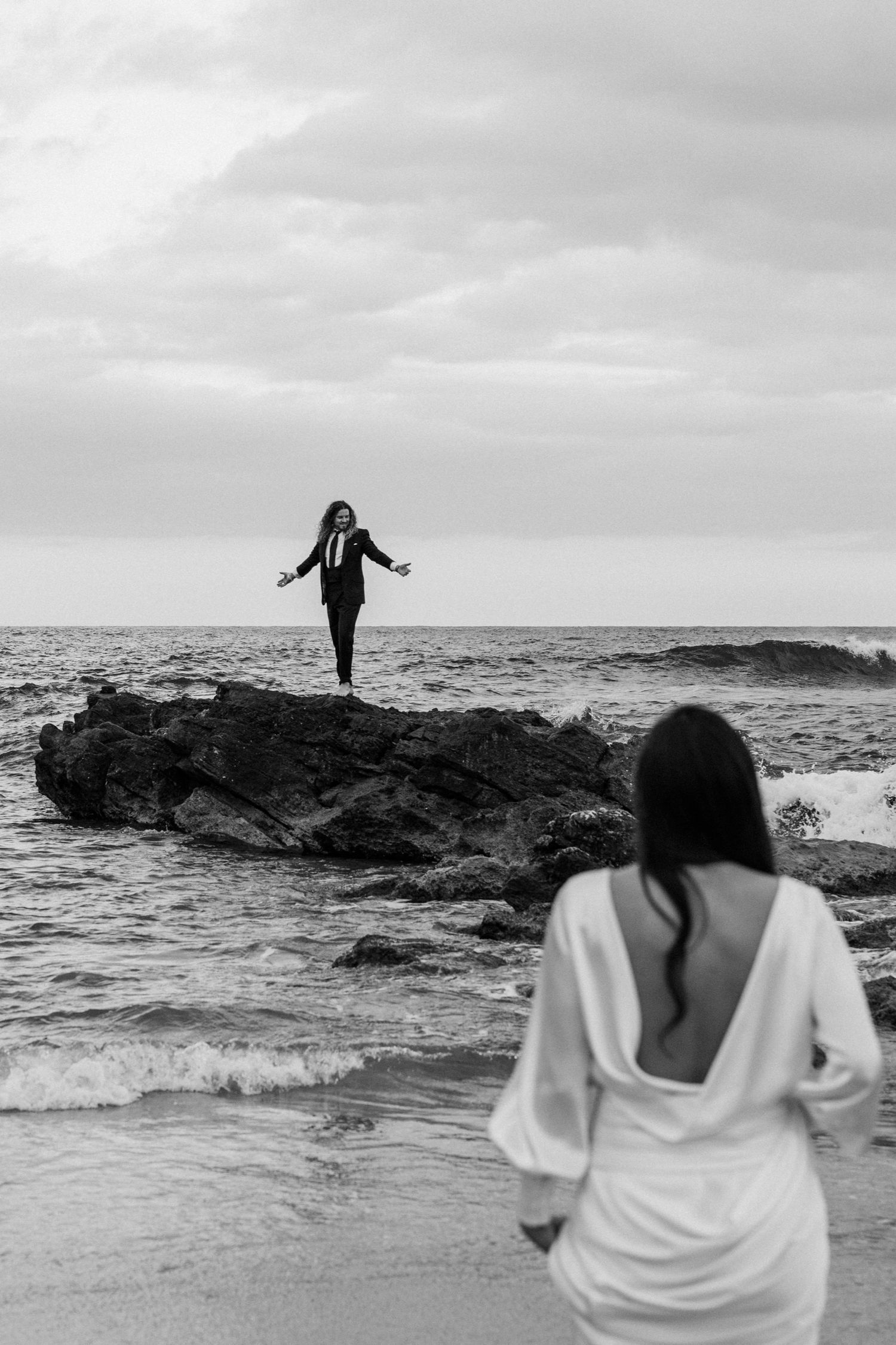 Dramatic black and white photo of two people on coastal rocks by ocean.