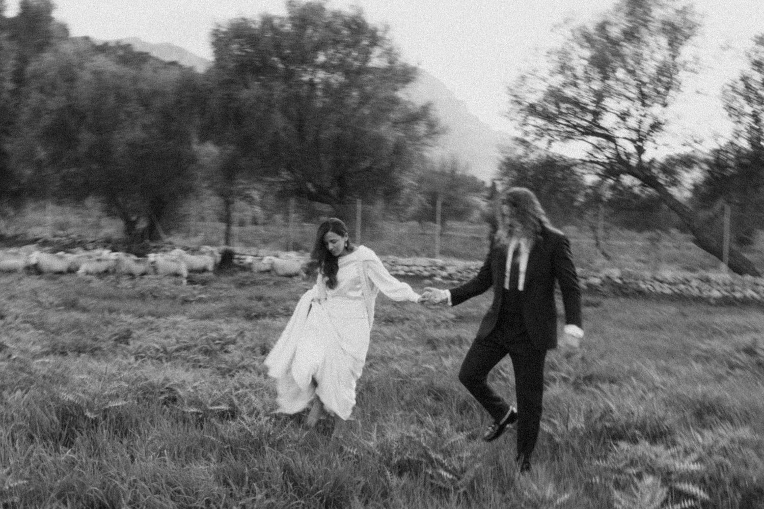 Black and white photograph of a couple walking through a pastoral countryside setting.