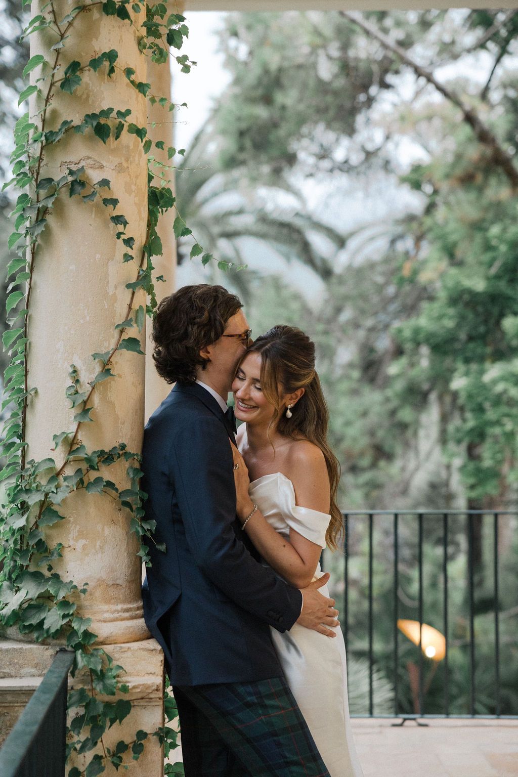 Wedding couple shares romantic moment against ivy-covered columns on Mediterranean terrace.
