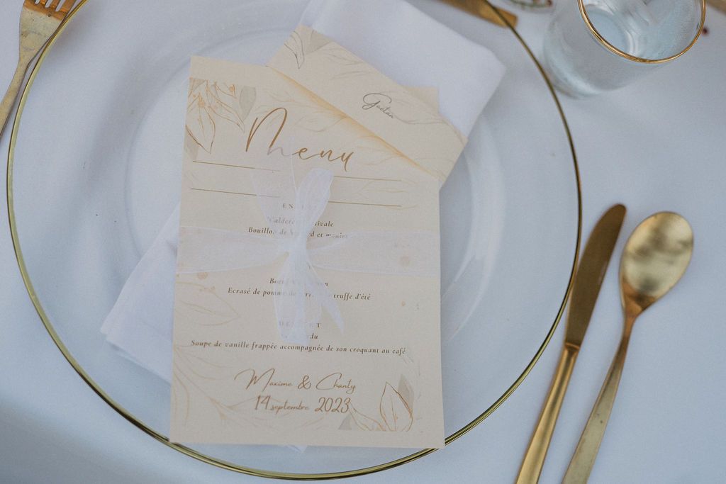 Close-up of elegant gold cutlery and place cards on white tablecloth at wedding reception.