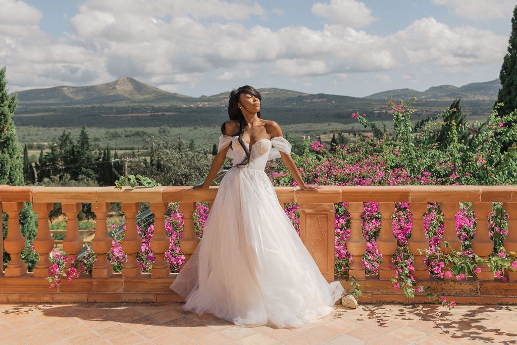 A stunning wedding dress silhouette against a mountain landscape with pink flowers on a terrace.