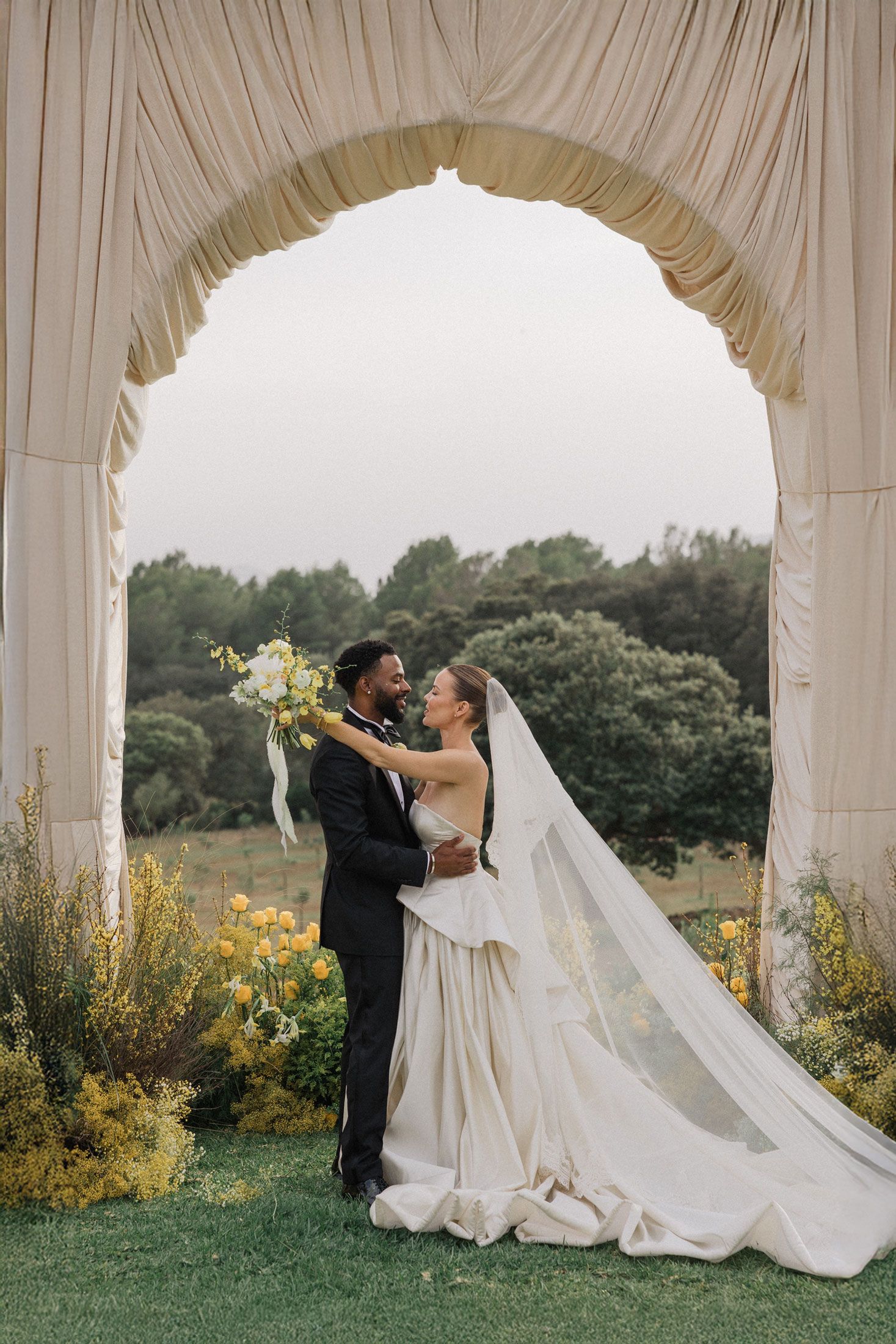 Romantic wedding couple dancing under an elegant white gazebo surrounded by gardens.