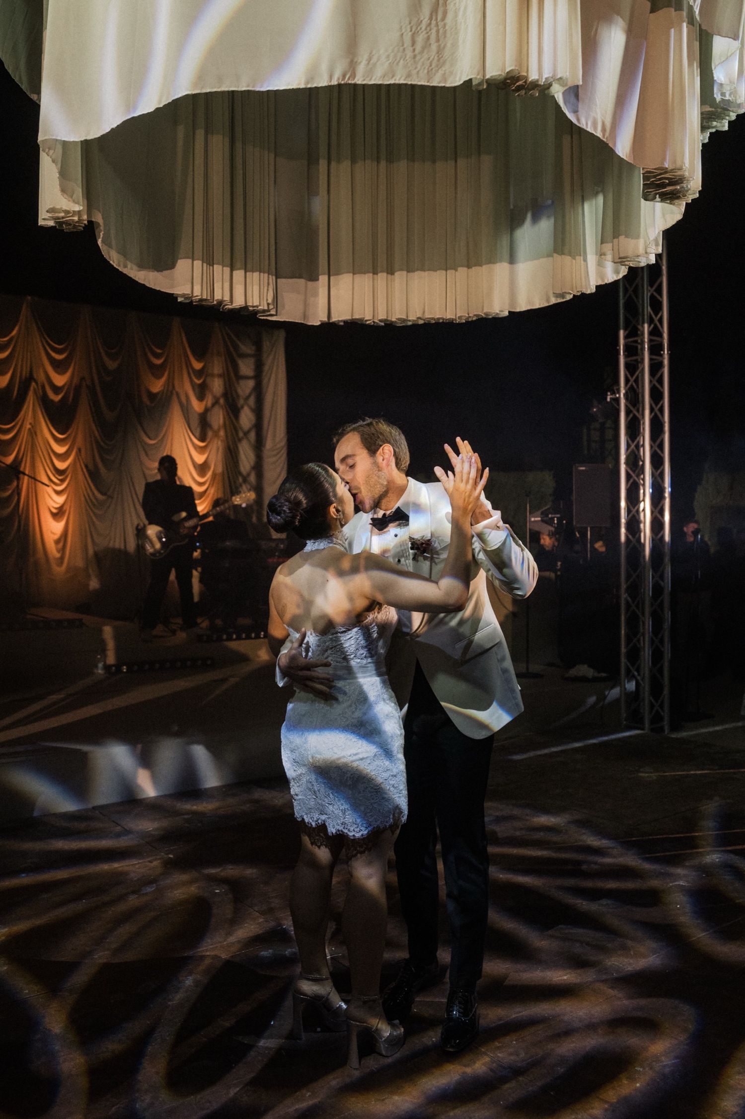 A couple performs a dramatic dance lift sequence in a dimly lit ballroom with draped curtains in the background.