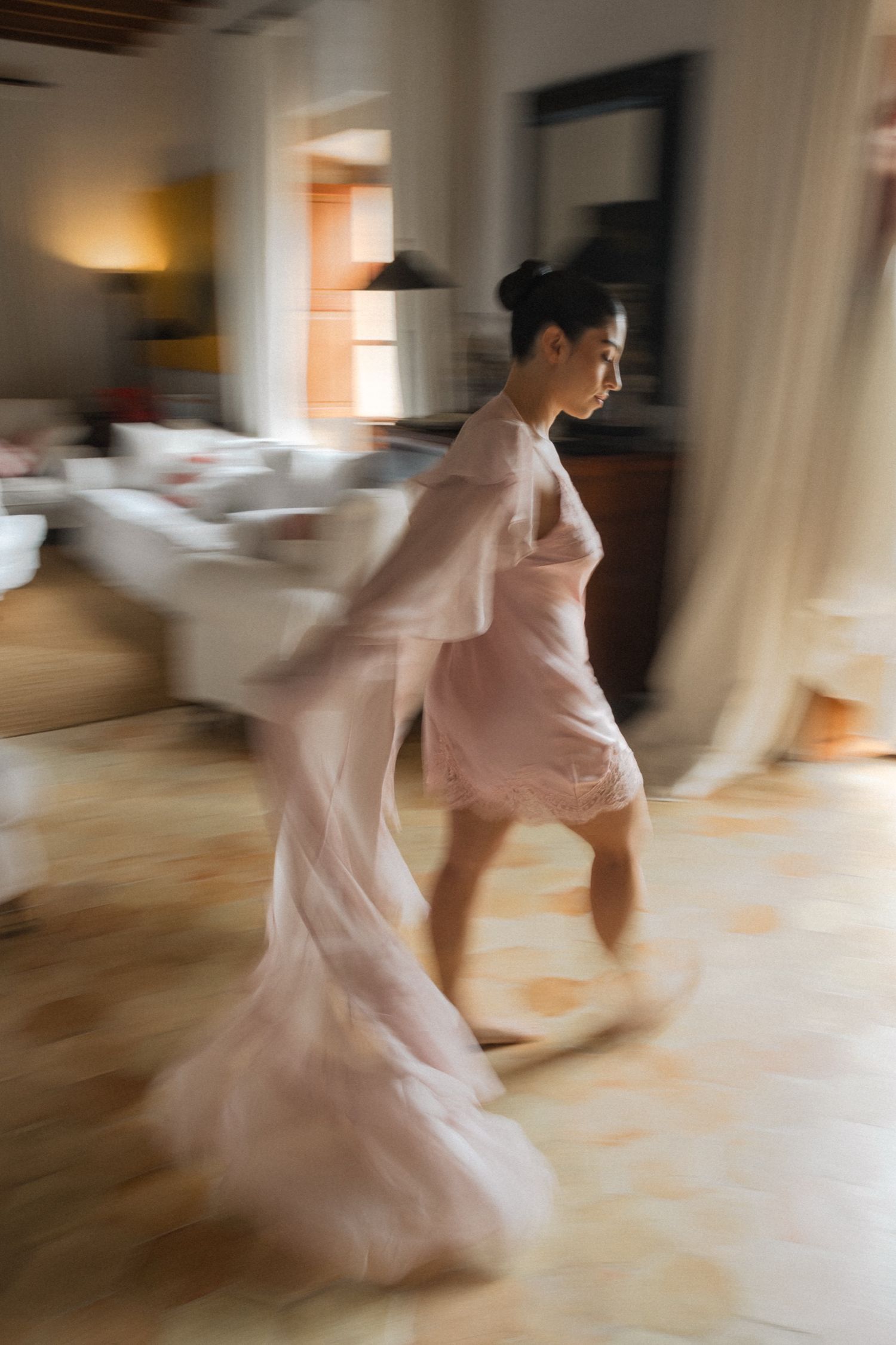 Motion blur sequence captures a figure in a flowing pink dress twirling and dancing across a sunlit room.